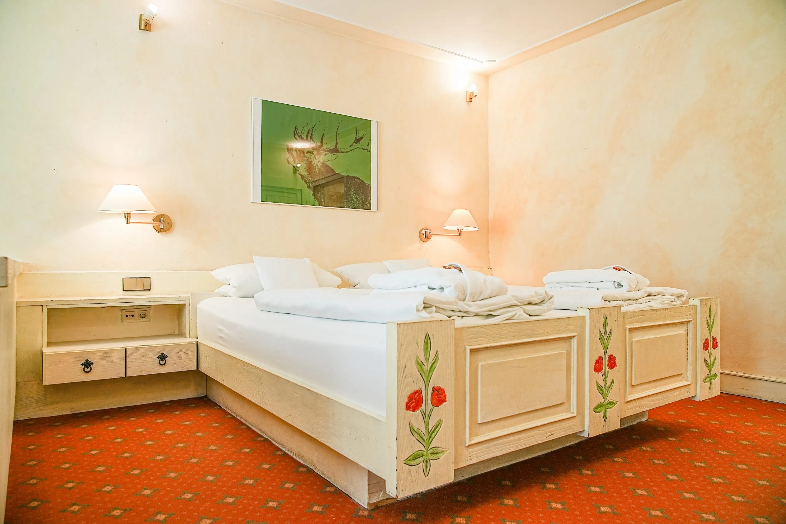 Zimmer mit cremefarbenen Bauernmöbeln, Doppelbett mit weißer Bettwäsche und rot gemustertem Teppichboden
