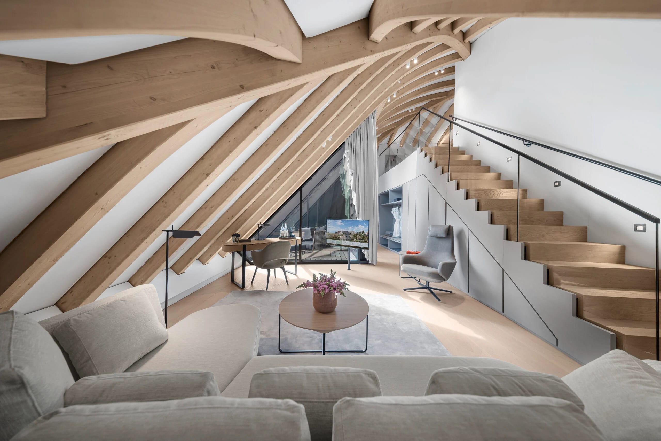 Wohnbereich einer Loft-Suite unter geschwungenen Holzsparren mit Sofa, Treppe zur Galerie und Arbeitsplatz