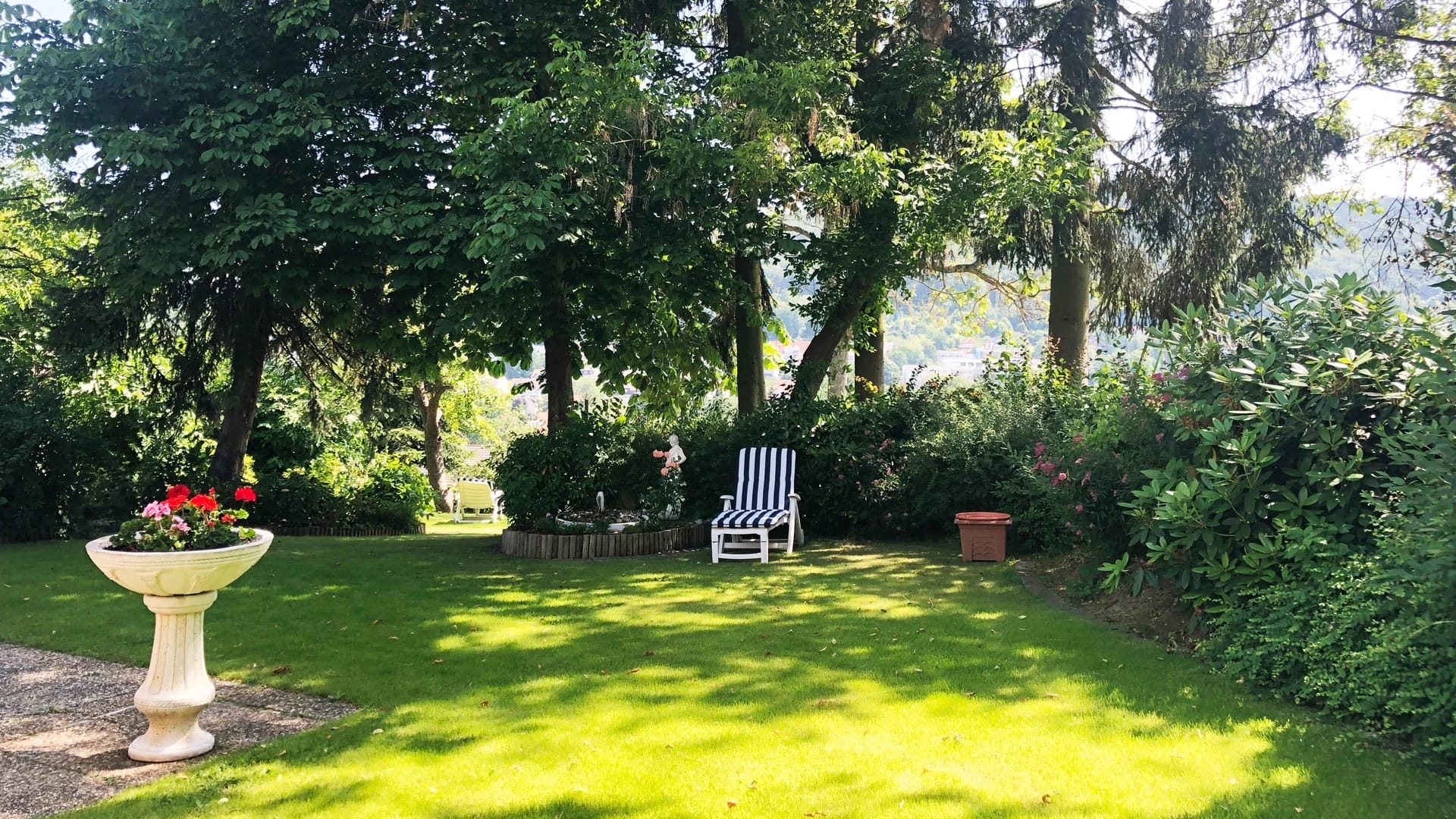 Gartenliege unter Bäumen mit Blick über den Ort