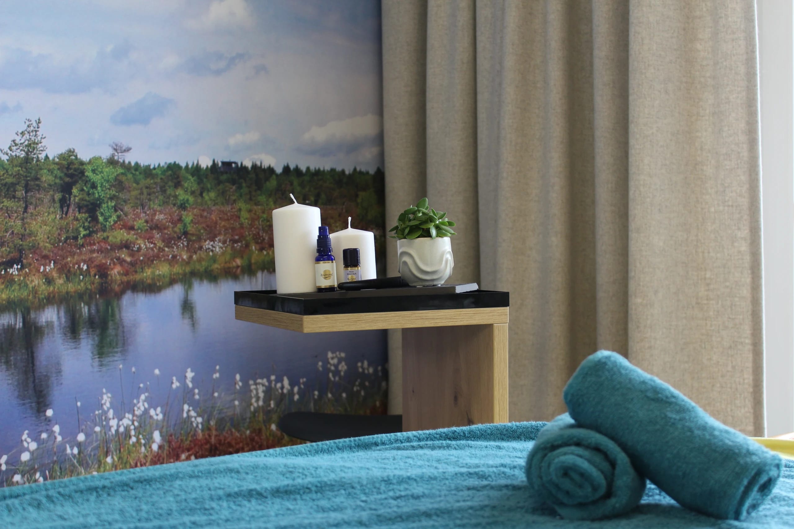 Behandlungsraum mit Massageliege, Handtüchern, Kerzen und Moorlandschaft als Fototapete