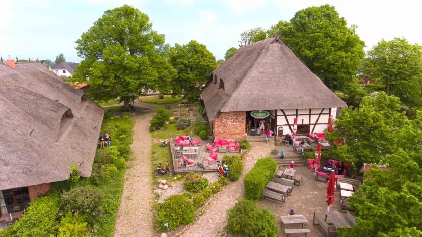 Luftaufnahme des Gutshofs mit reetgedeckten Häusern, Innenhof und altem Baumbestand