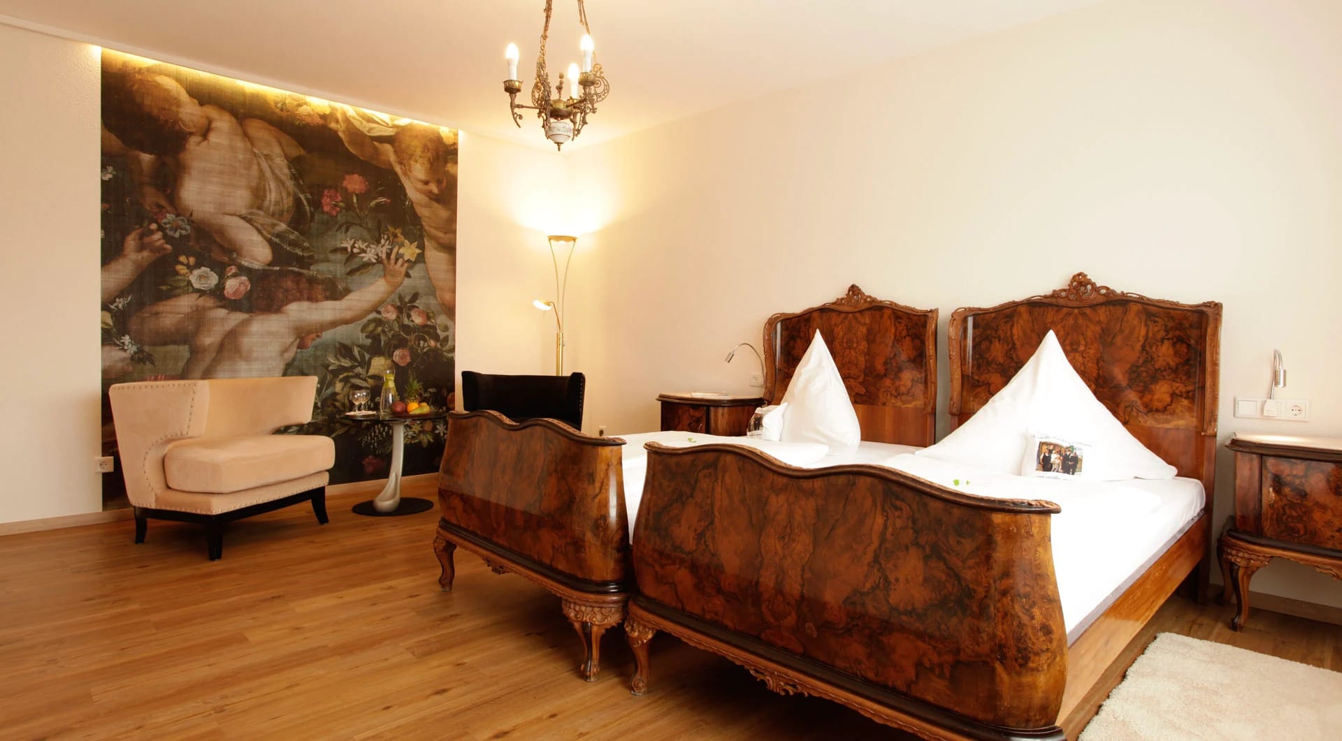 Themenzimmer mit zwei verzierten Holzbetten, Kronleuchter und großformatigem Wandbild