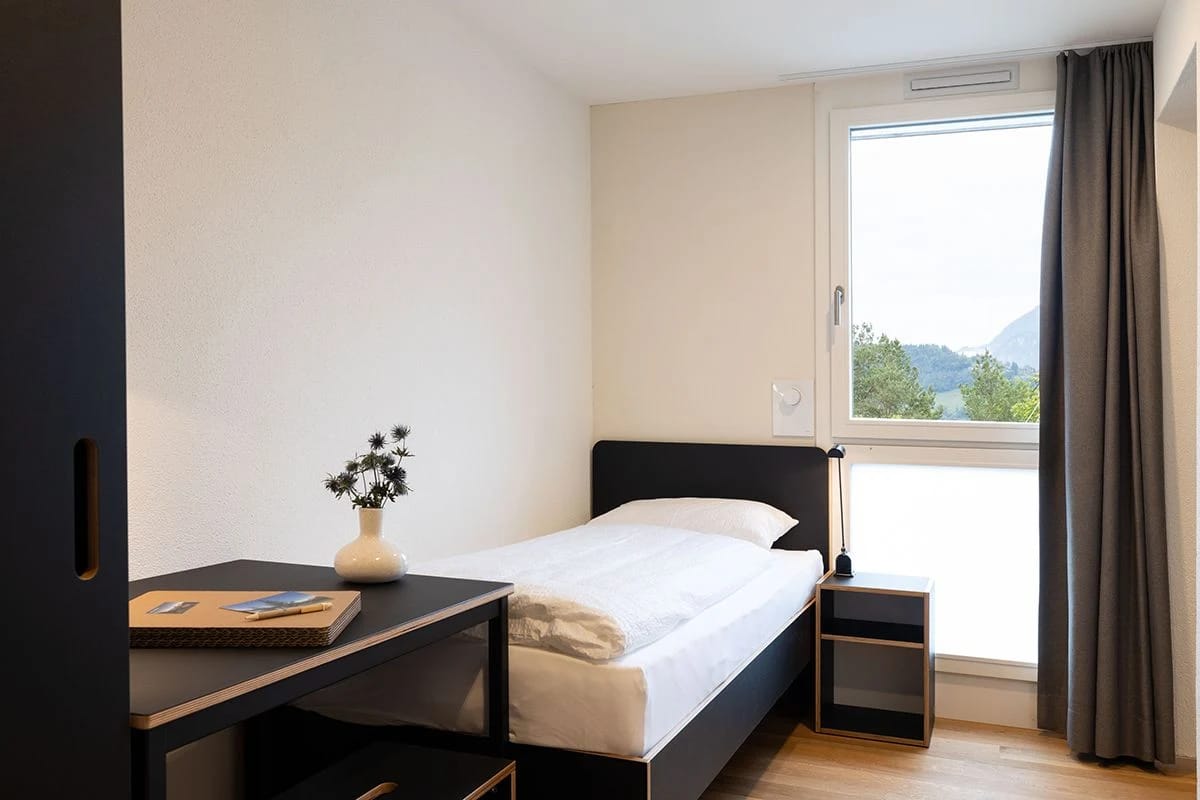 Einzelzimmer mit Schreibtisch, Nachttisch und Fenster mit Blick ins Grüne