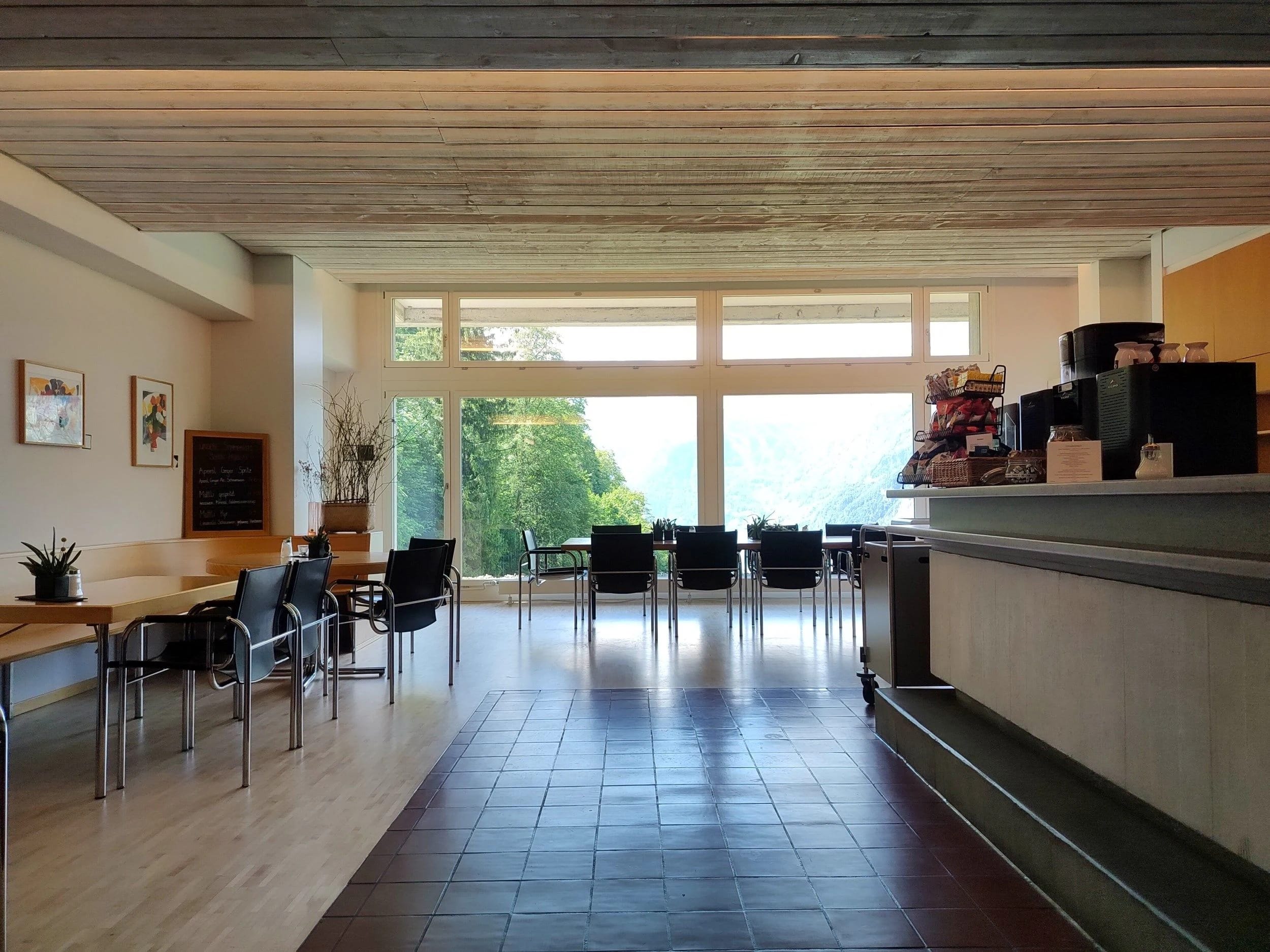 Restaurantraum mit Holzdecke, Tischen und Stühlen und großen Fenstern ins Grüne