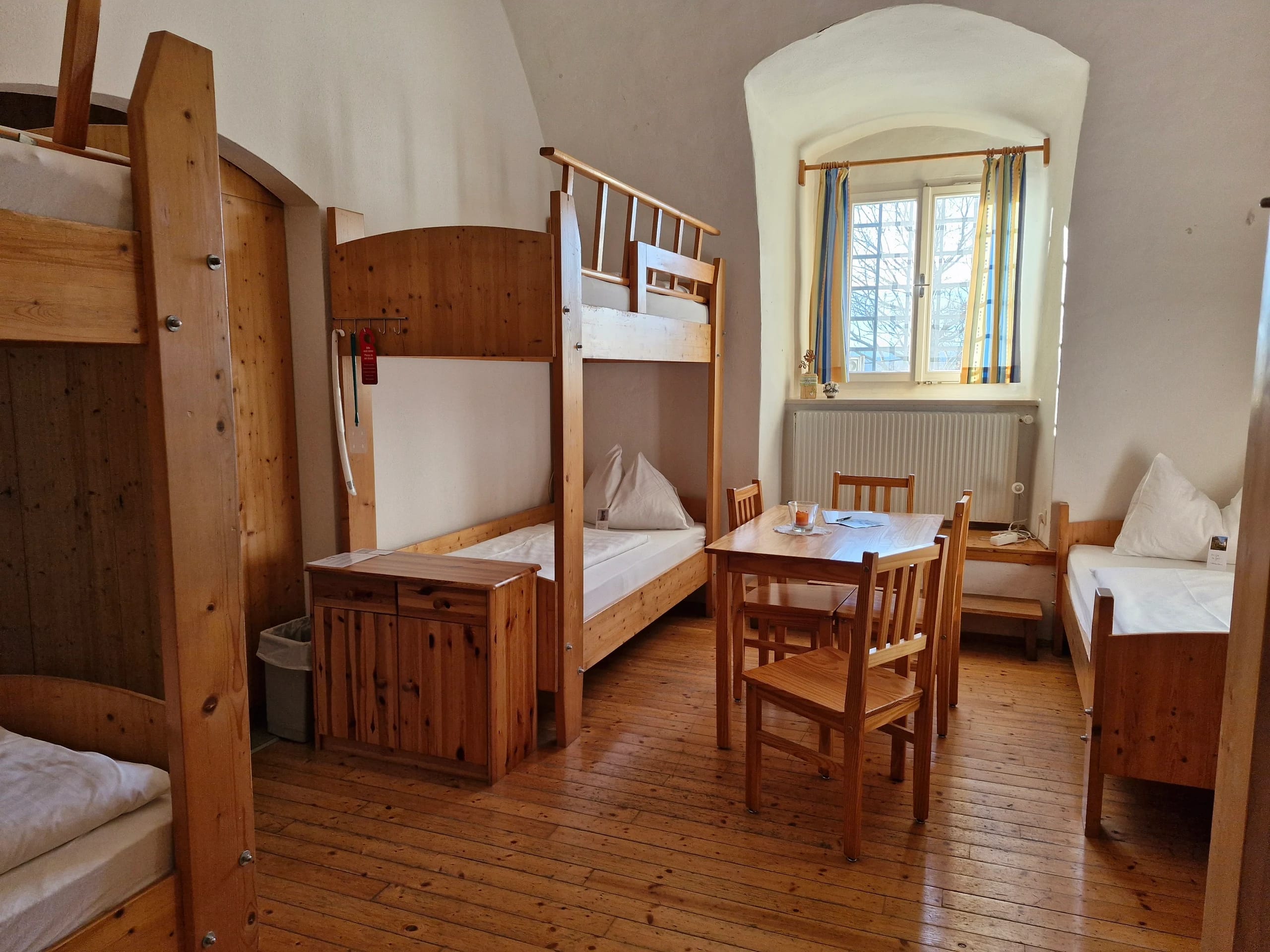 Mehrbettzimmer unter Gewölbedecke mit Stockbetten, Einzelbett und Tisch mit Stühlen