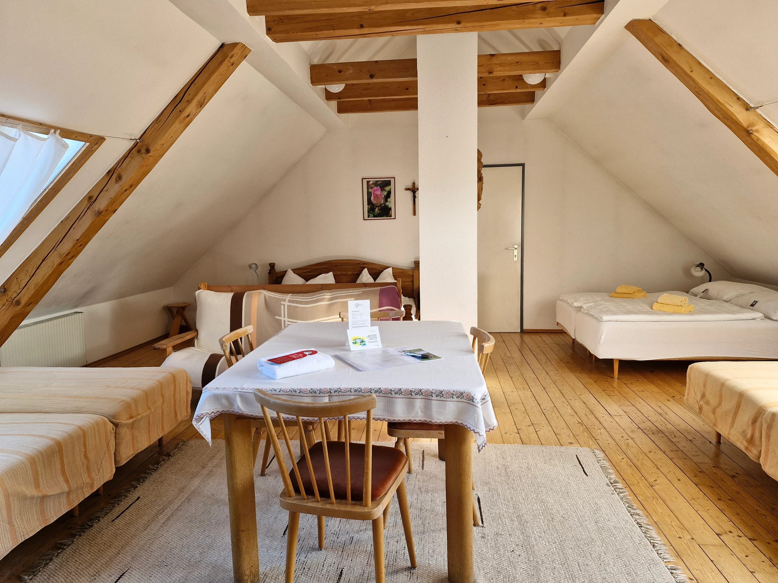 Helles Dachzimmer mit Holzbalken, Doppelbett, zwei Einzelbetten und Tisch mit Stühlen