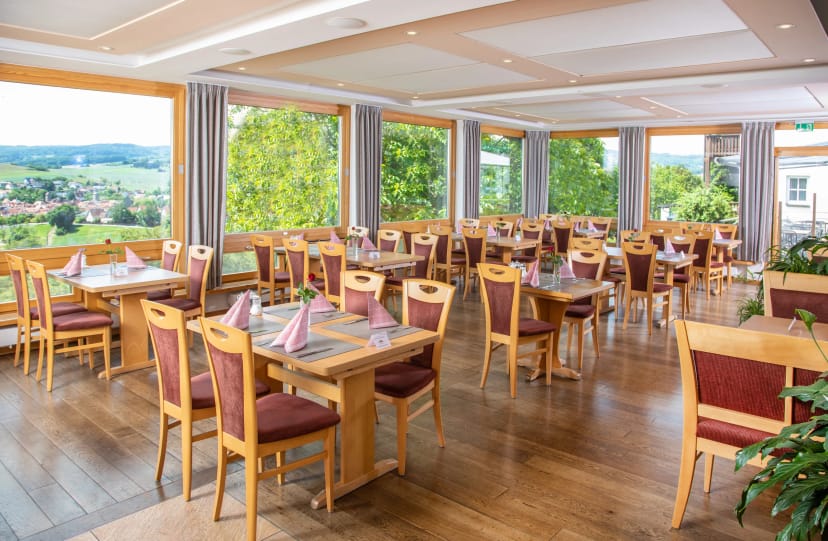 Panoramarestaurant mit Holztischen, Stoffservietten und umlaufender Fensterfront ins Grüne