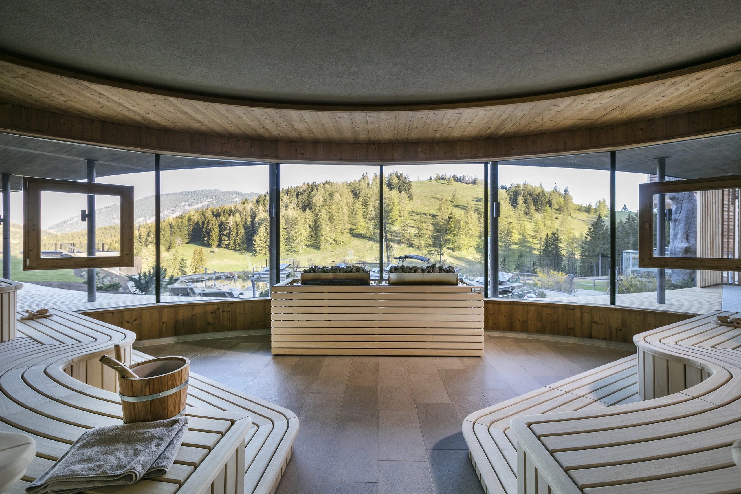 Runde Panoramasauna aus Holz mit umlaufenden Fenstern und Blick auf Wiesen und Wald