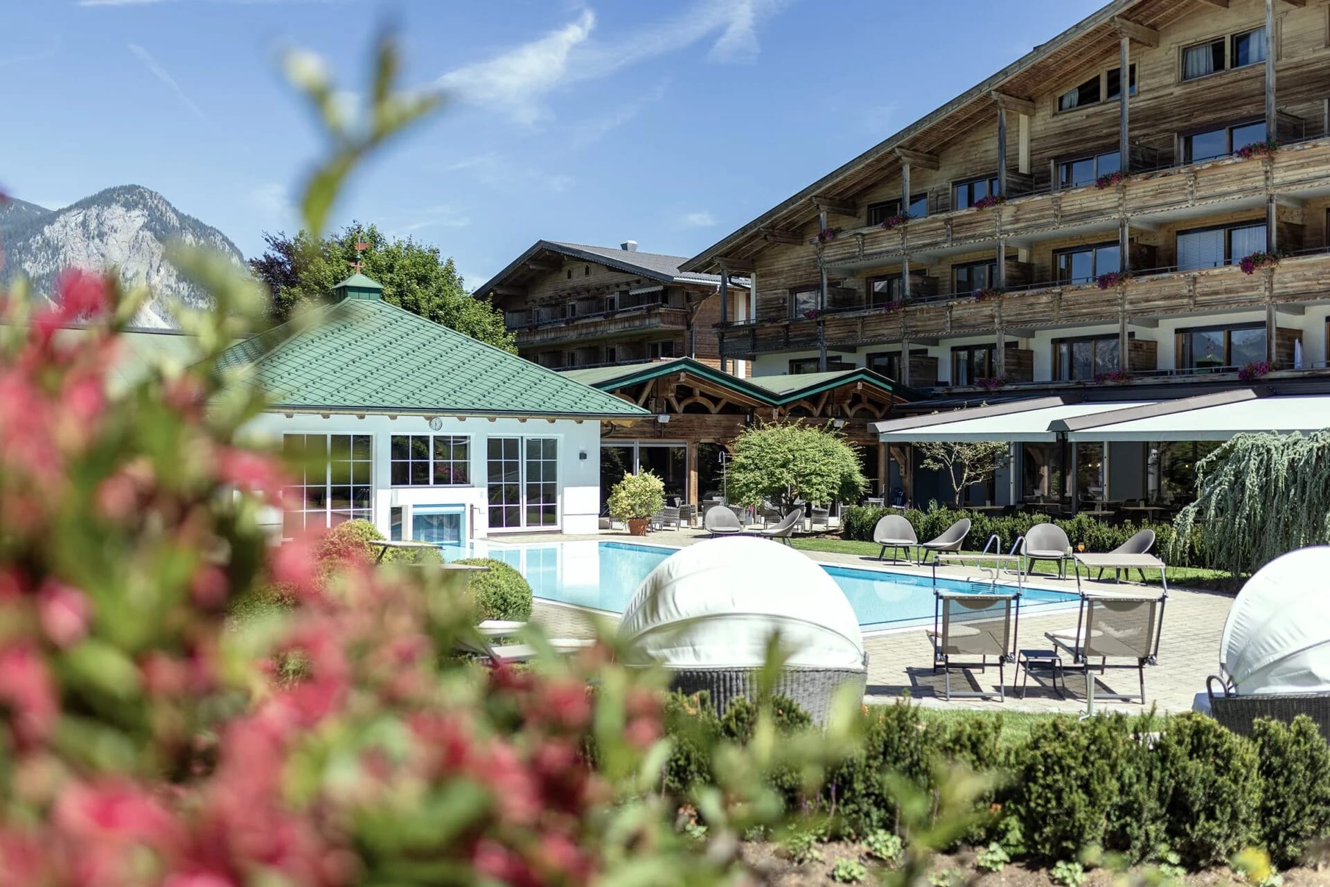 Außenpool des Hotel Pirchnerhof mit Sonnenliegen, Poolhaus und Hotelgebäude im Hintergrund