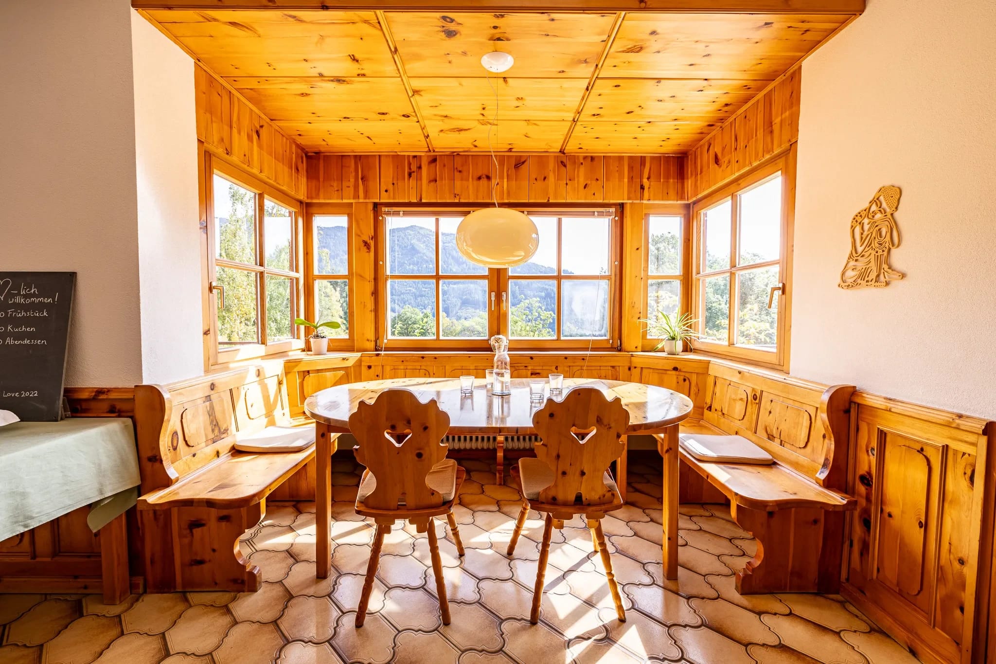 Holzvertäfelter Erker mit runder Tafel, Eckbank und geschnitzten Stühlen vor Fenstern mit Bergblick