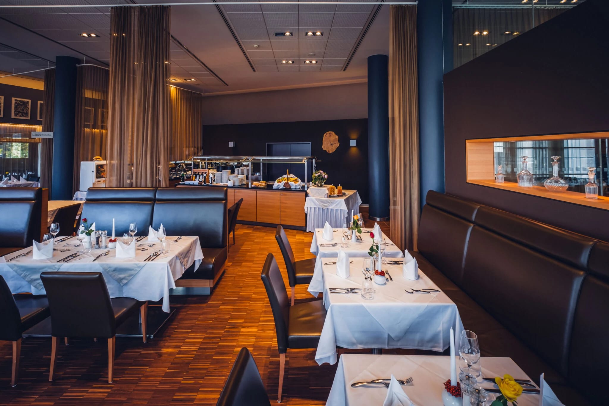 Restaurant mit eingedeckten Tischen, dunklen Polsterbänken und Holzboden