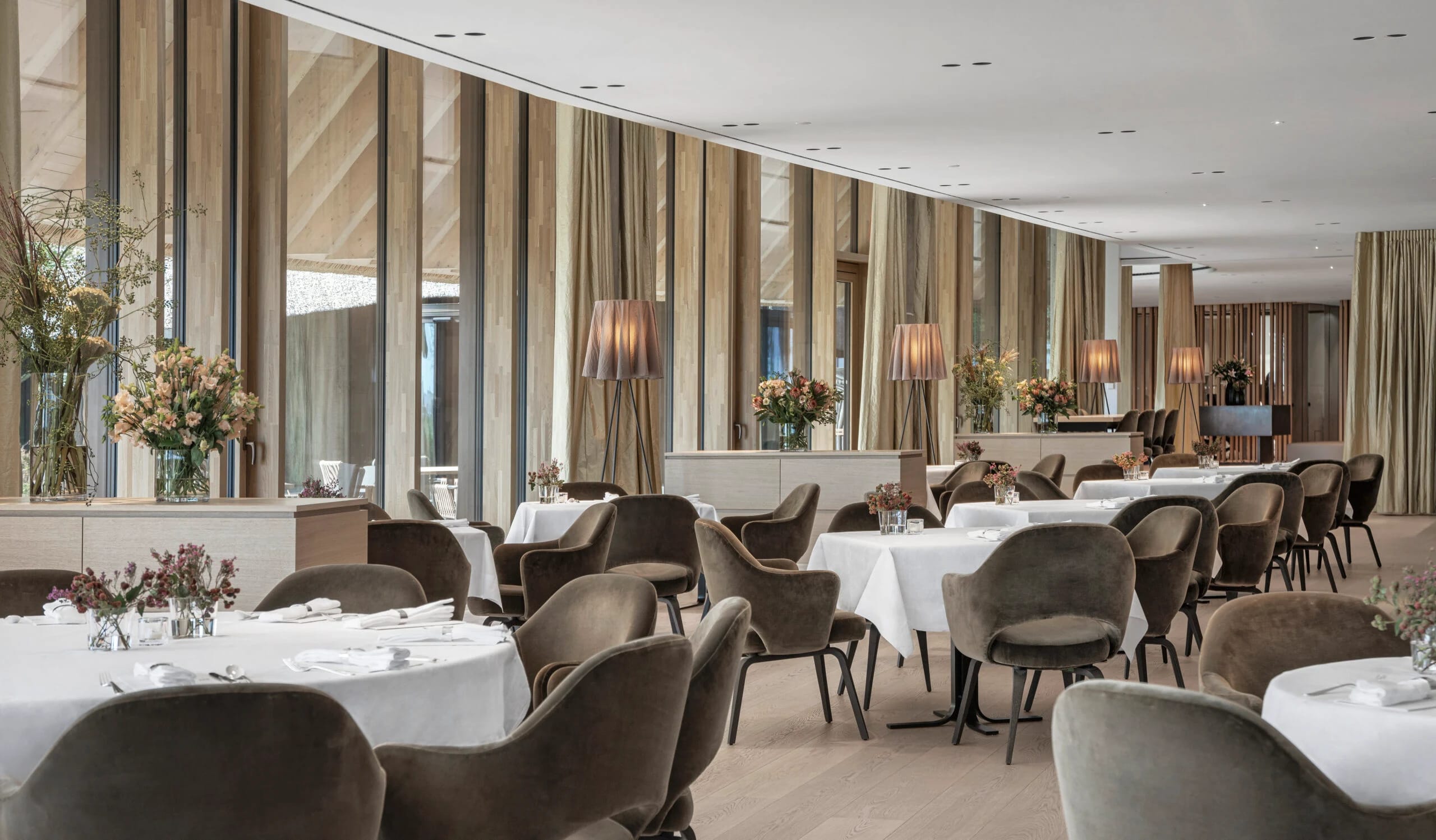 Restaurant mit eingedeckten runden Tischen, Polsterstühlen und Blumenschmuck