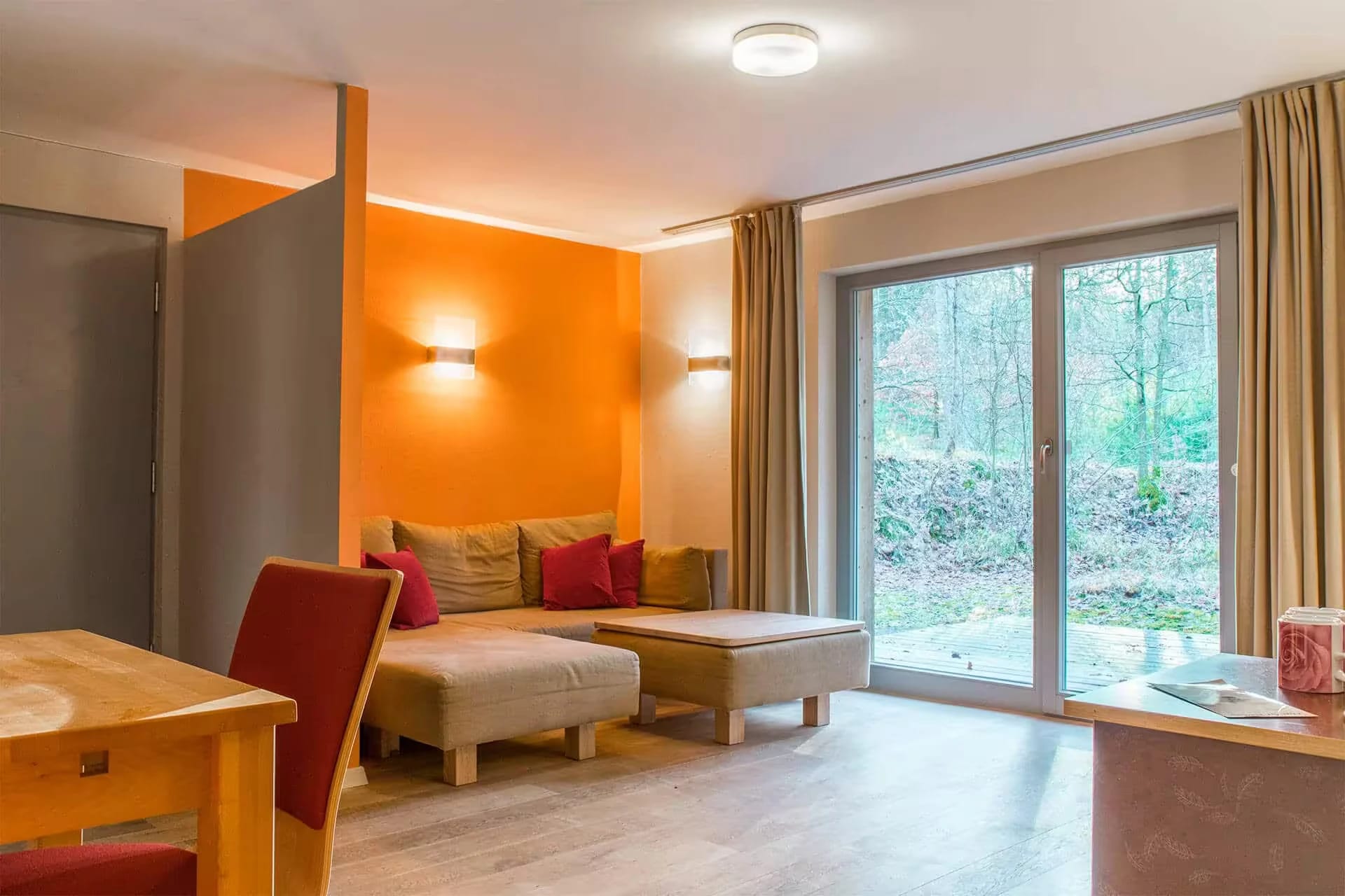 Wohnraum eines Waldhäuschens mit Sofa und bodentiefer Fensterfront zum Wald