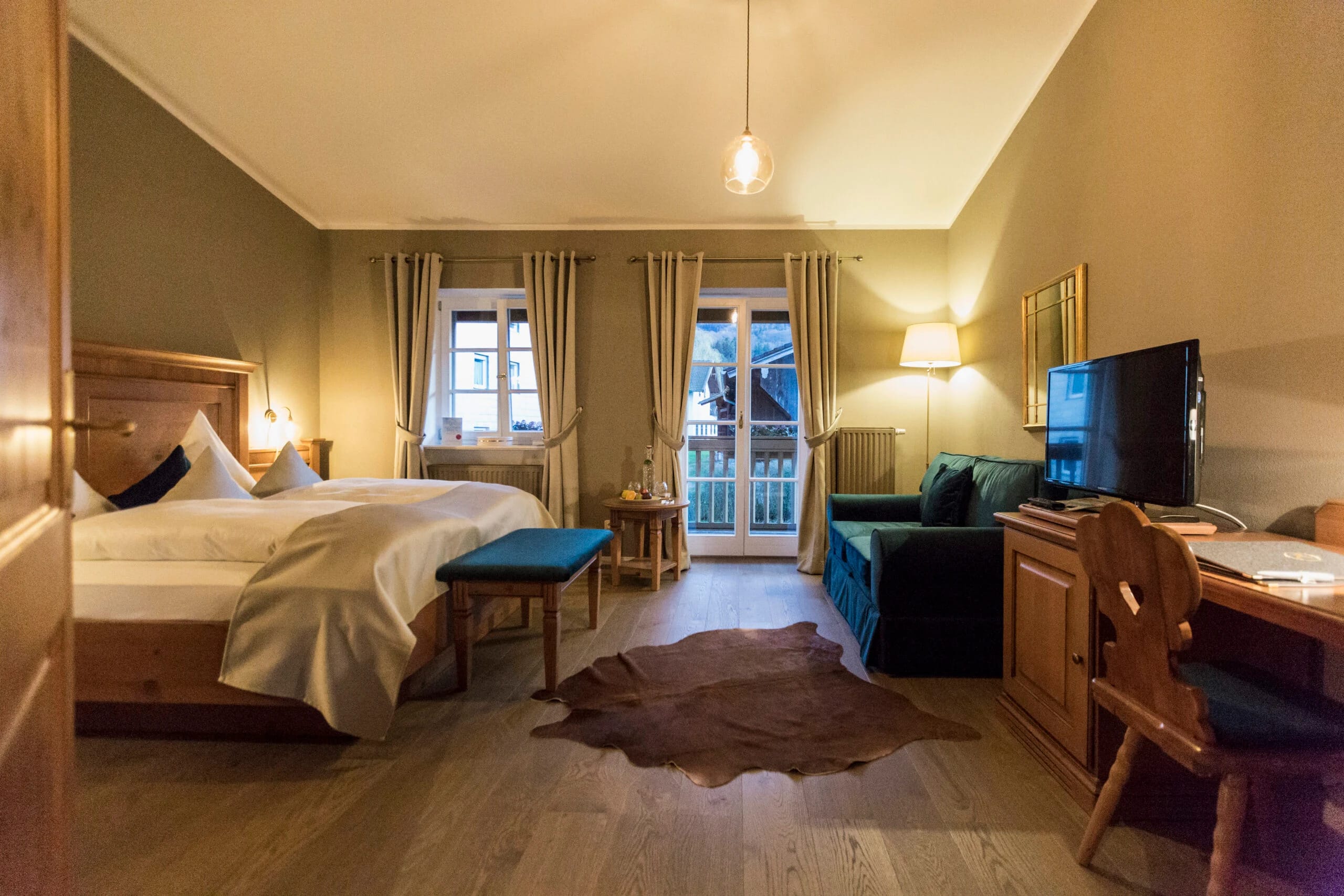 Zimmer mit Doppelbett, grünem Sofa und Fellteppich vor Balkontür