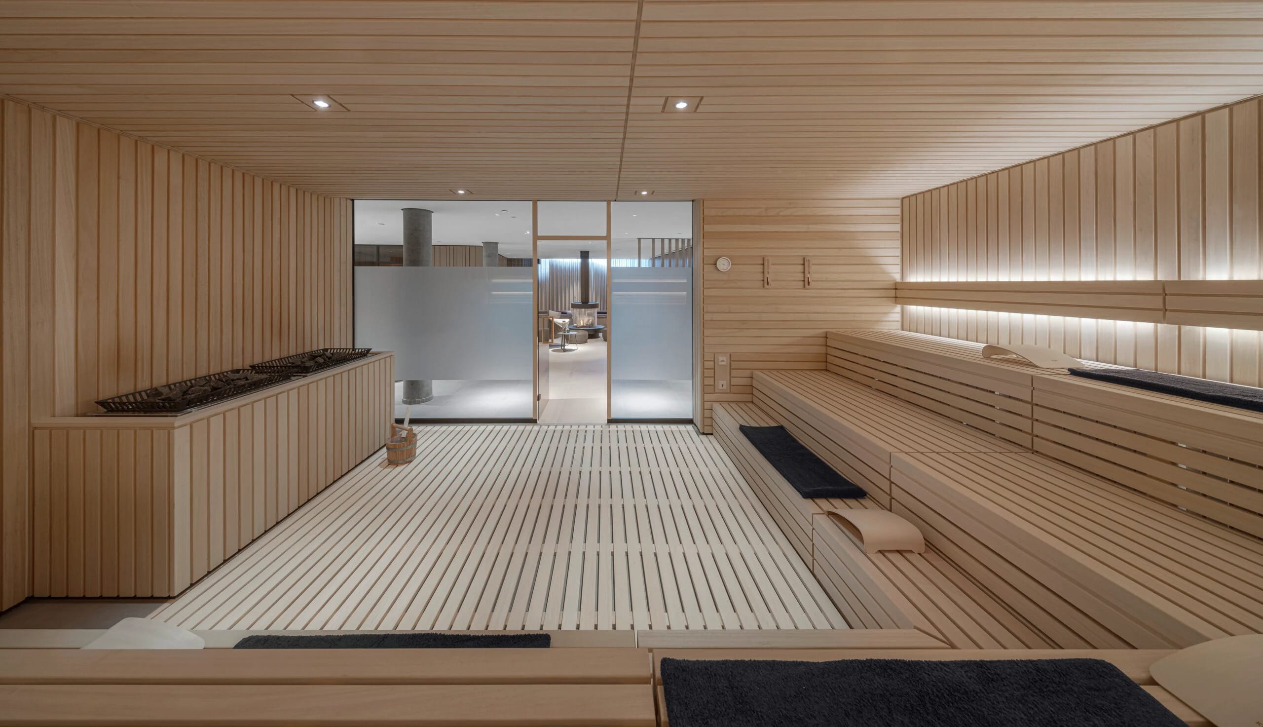 Holzsauna mit umlaufenden Bänken, Saunaofen und dunklen Handtüchern