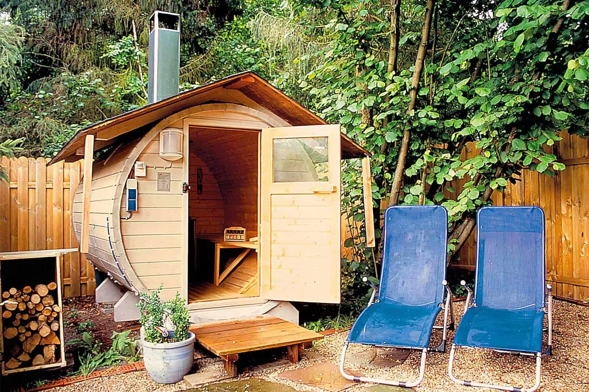 Fasssauna aus Holz im Garten mit zwei Liegestühlen davor