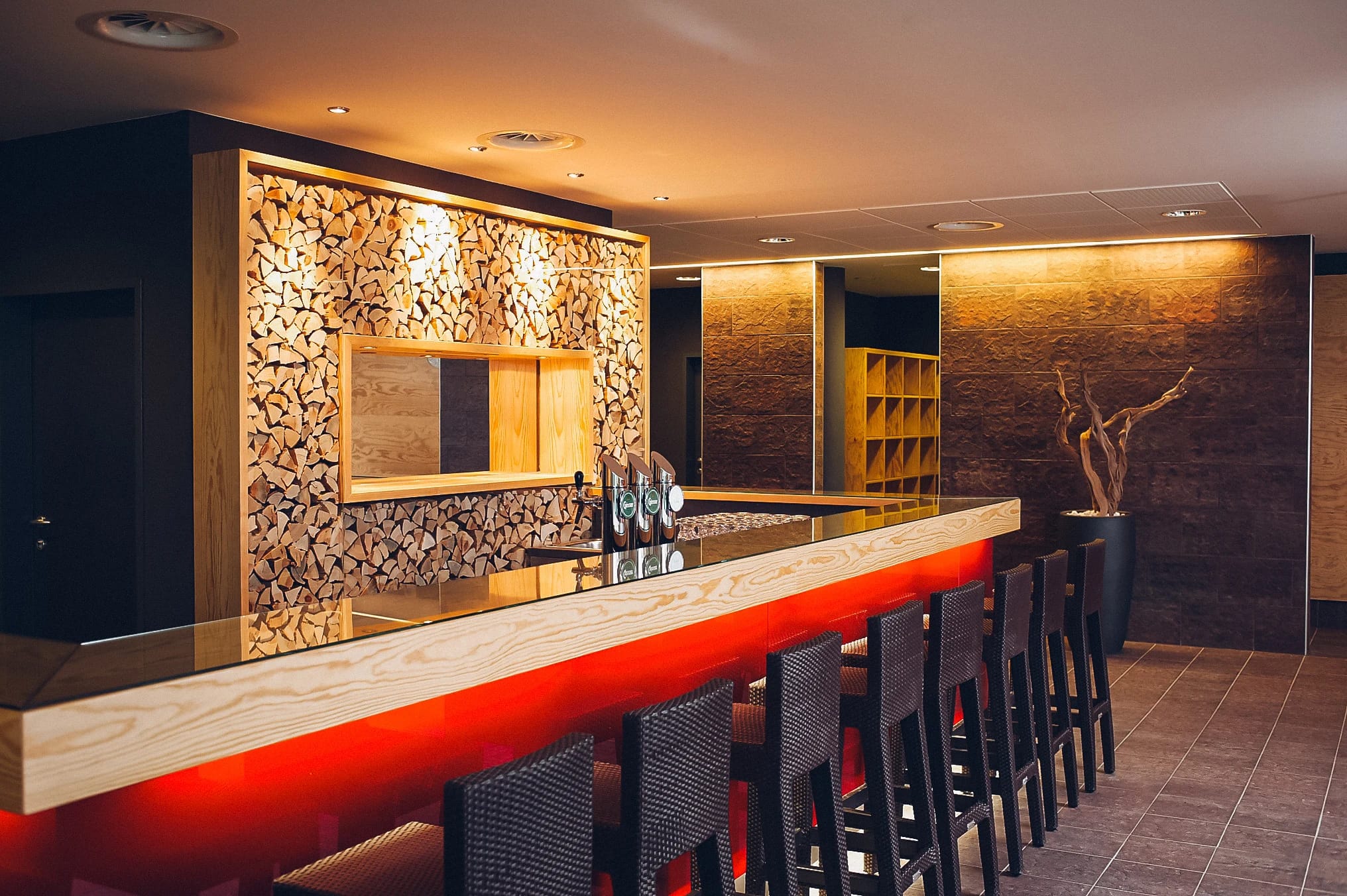 Bar mit Barhockern, warmem Licht und einer Wand aus geschlichtetem Brennholz