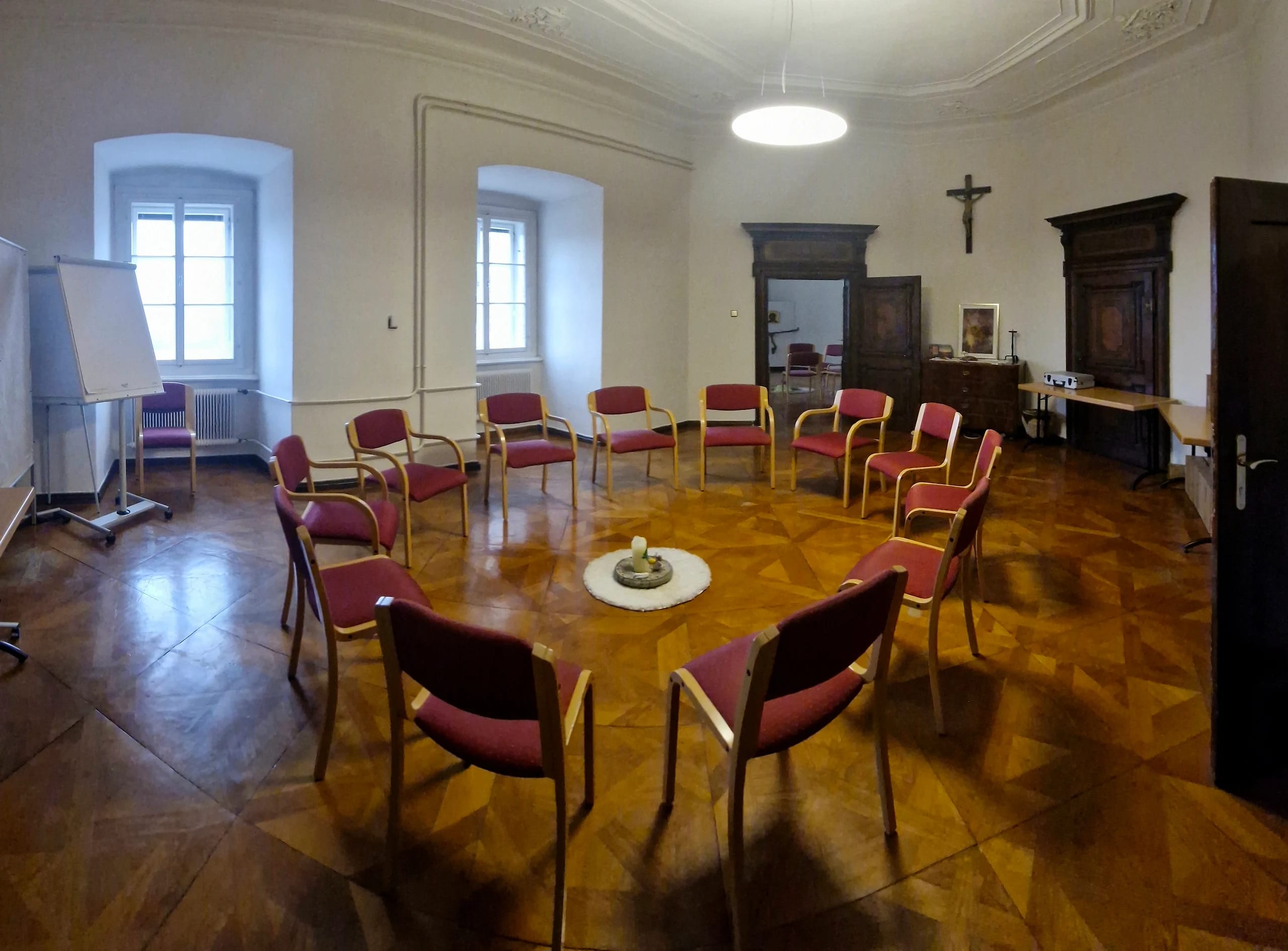 Seminarraum mit Stuhlkreis, Parkettboden, Flipchart und historischen Holzschränken