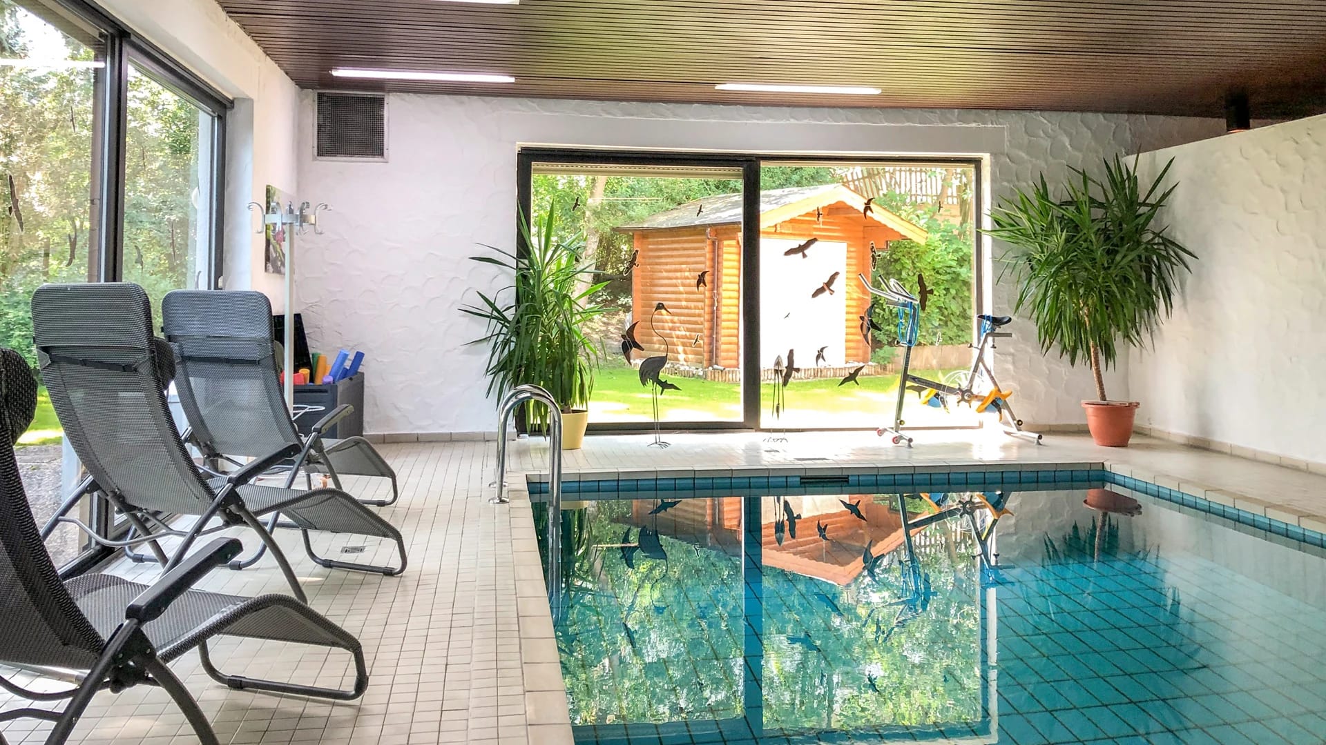 Hallenbad mit Liegen und großem Fenster zum Garten