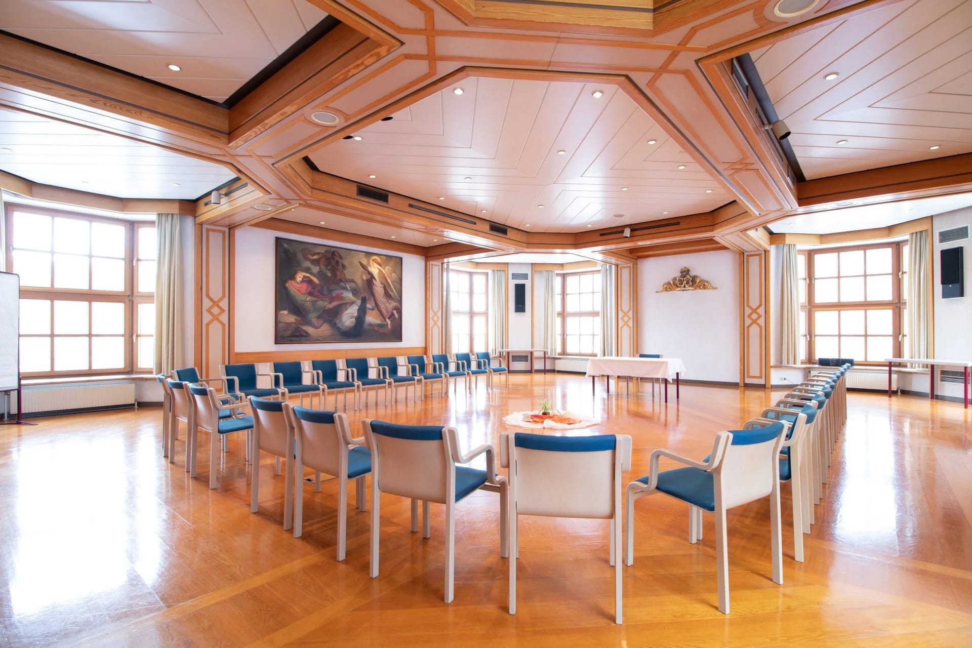 Holzvertäfelter Saal mit Kassettendecke, großer Tafel und hellen Polsterstühlen