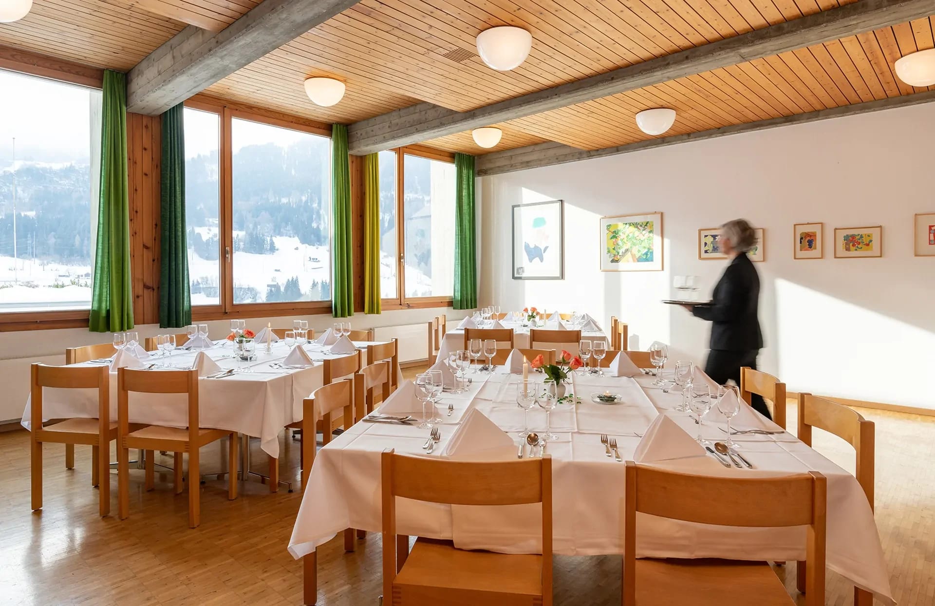Saal mit eingedeckten Tischen, Holzdecke und Fensterfront mit Blick ins Tal