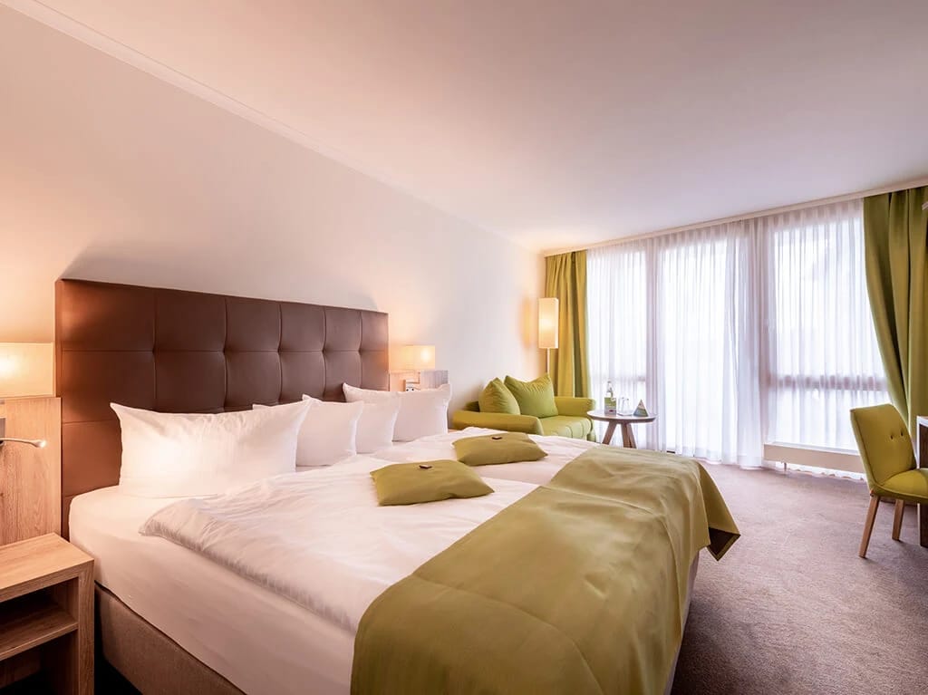 Doppelzimmer mit gepolstertem Kopfteil, Sessel und bodentiefem Fenster
