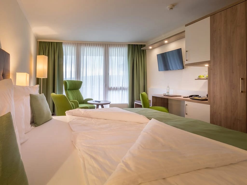 Doppelzimmer mit grünen Vorhängen, Sessel und Flachbildfernseher