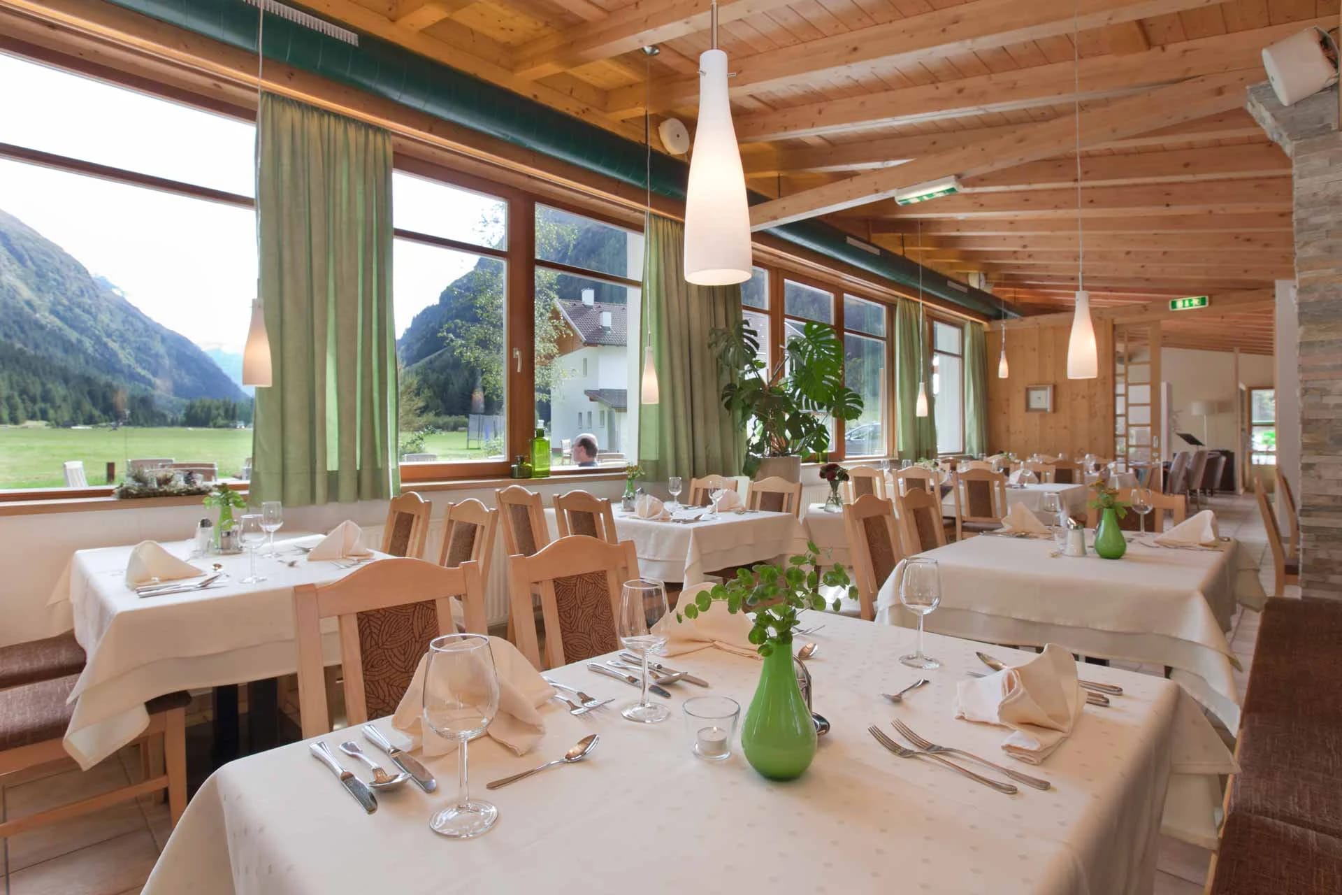 Speisesaal mit eingedeckten Tischen und Fensterfront mit Blick ins Tal