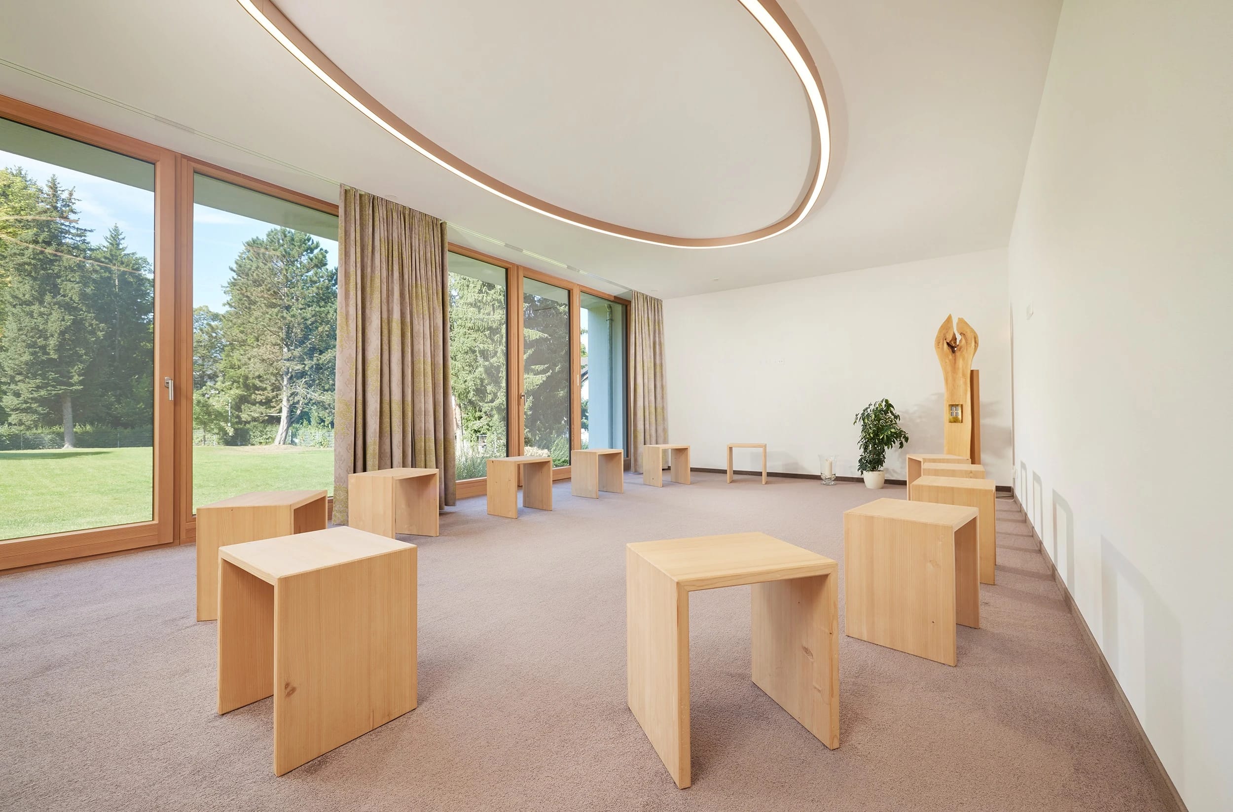 Raum der Stille mit schlichten Holzhockern und großen Fenstern ins Grüne