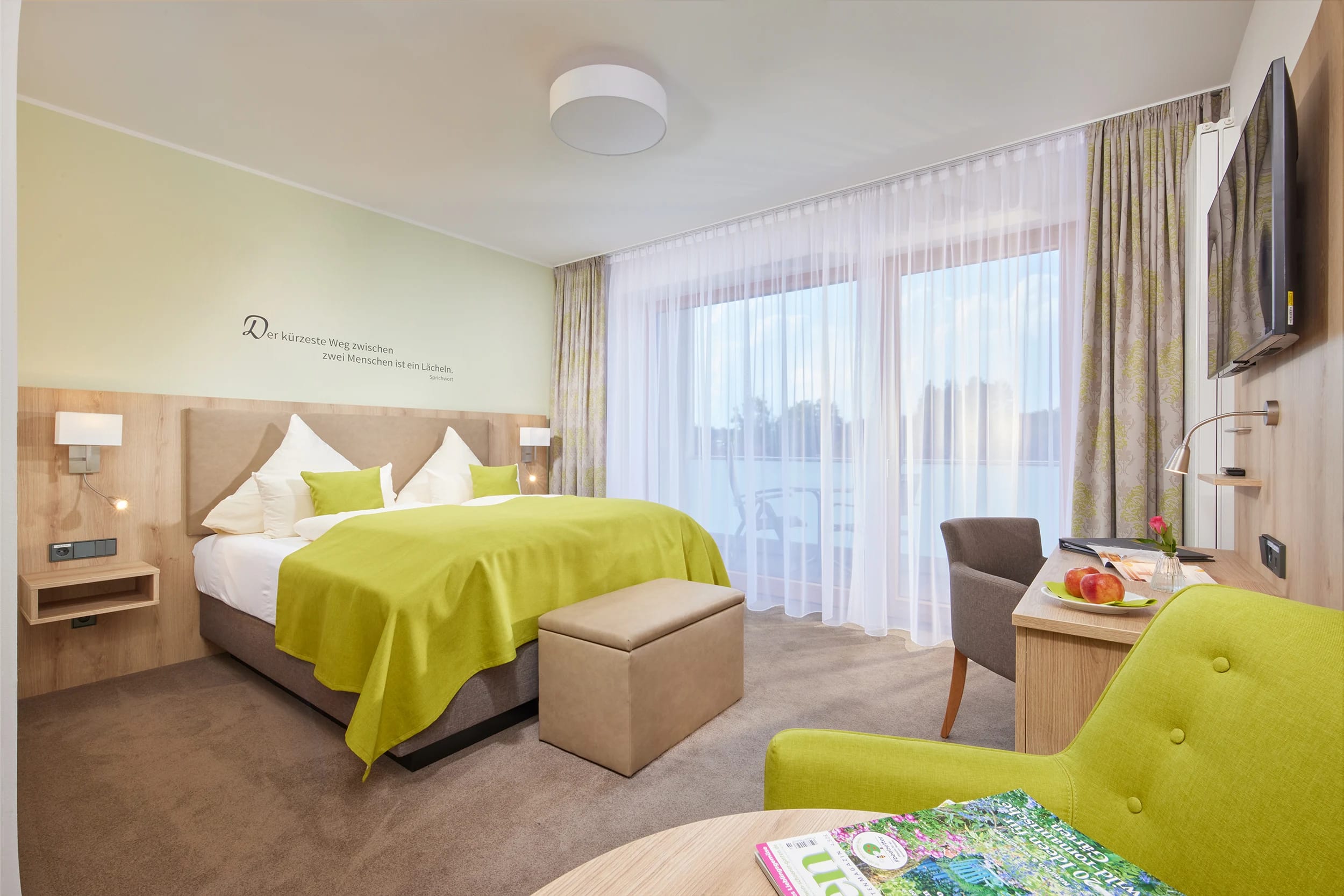 Zimmer mit Bett, Sesseln und bodentiefer Fenstertür zum Balkon