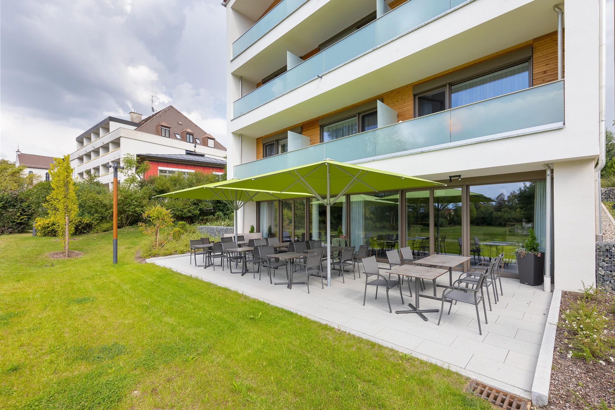 Terrasse mit Tischen, Stühlen und Sonnenschirm vor dem Haus, umgeben von Rasen