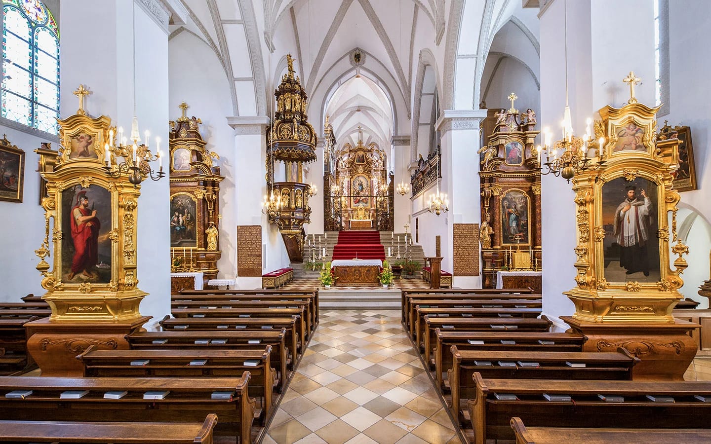 Innenraum der Stiftskirche mit vergoldeten Seitenaltären und Kirchenbänken