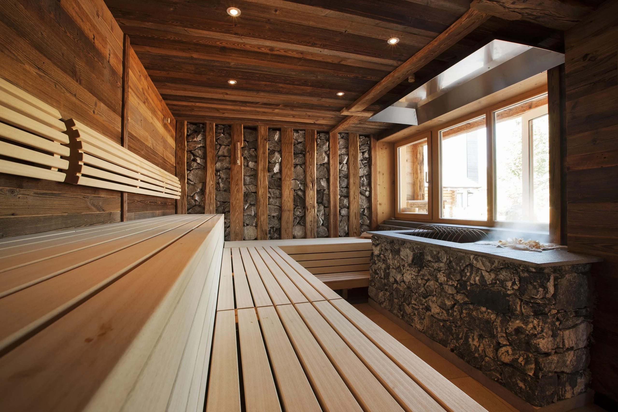 Stollensauna mit Holzbänken, Natursteinwand aus Magnesitstein und Fenster