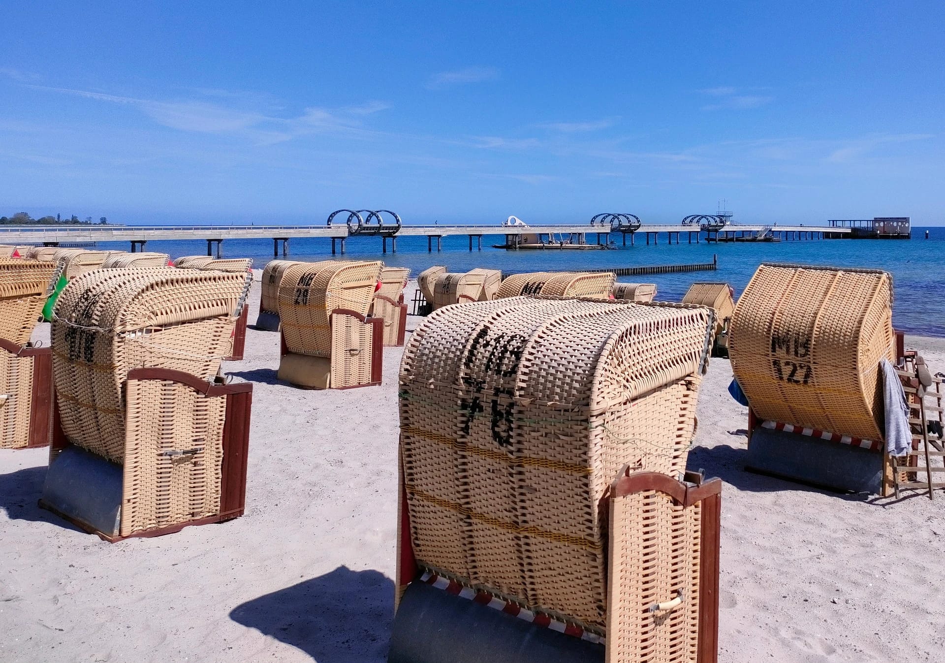Strandkörbe am Sandstrand mit Seebrücke im Hintergrund