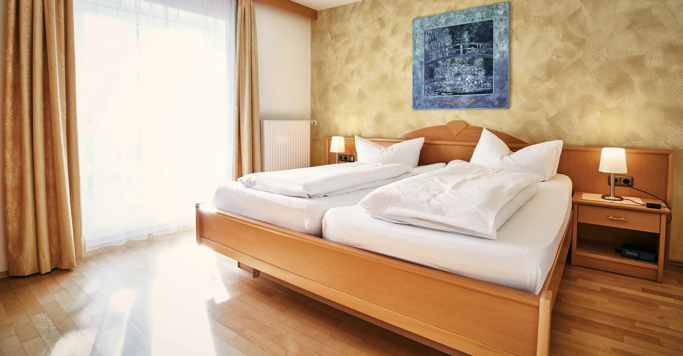 Helles Doppelzimmer mit Holzbett, Nachttischlampen und sonnendurchflutetem Fenster