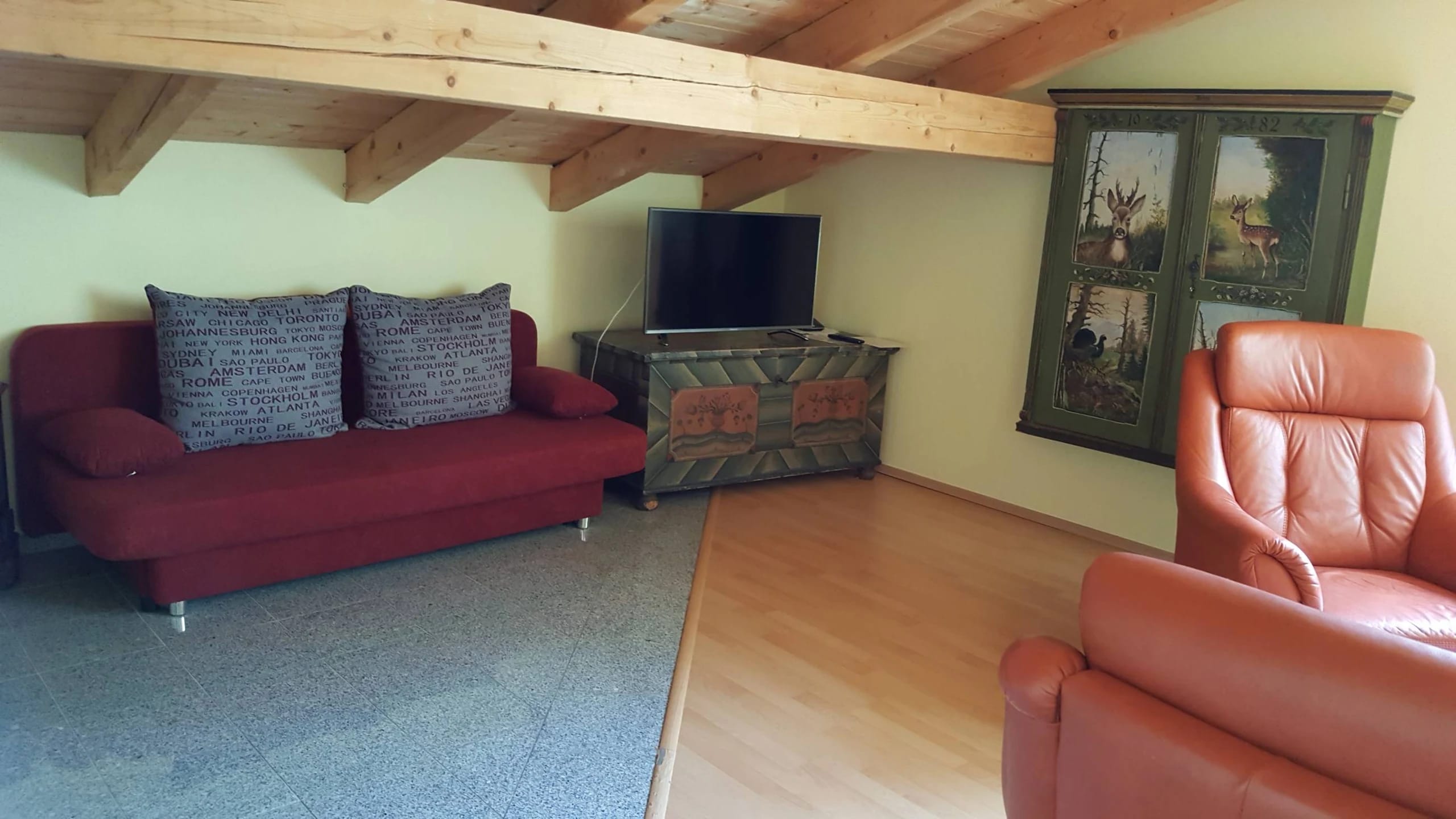 Wohnbereich der Suite mit roter Couch, Ledersessel und Holzbalkendecke