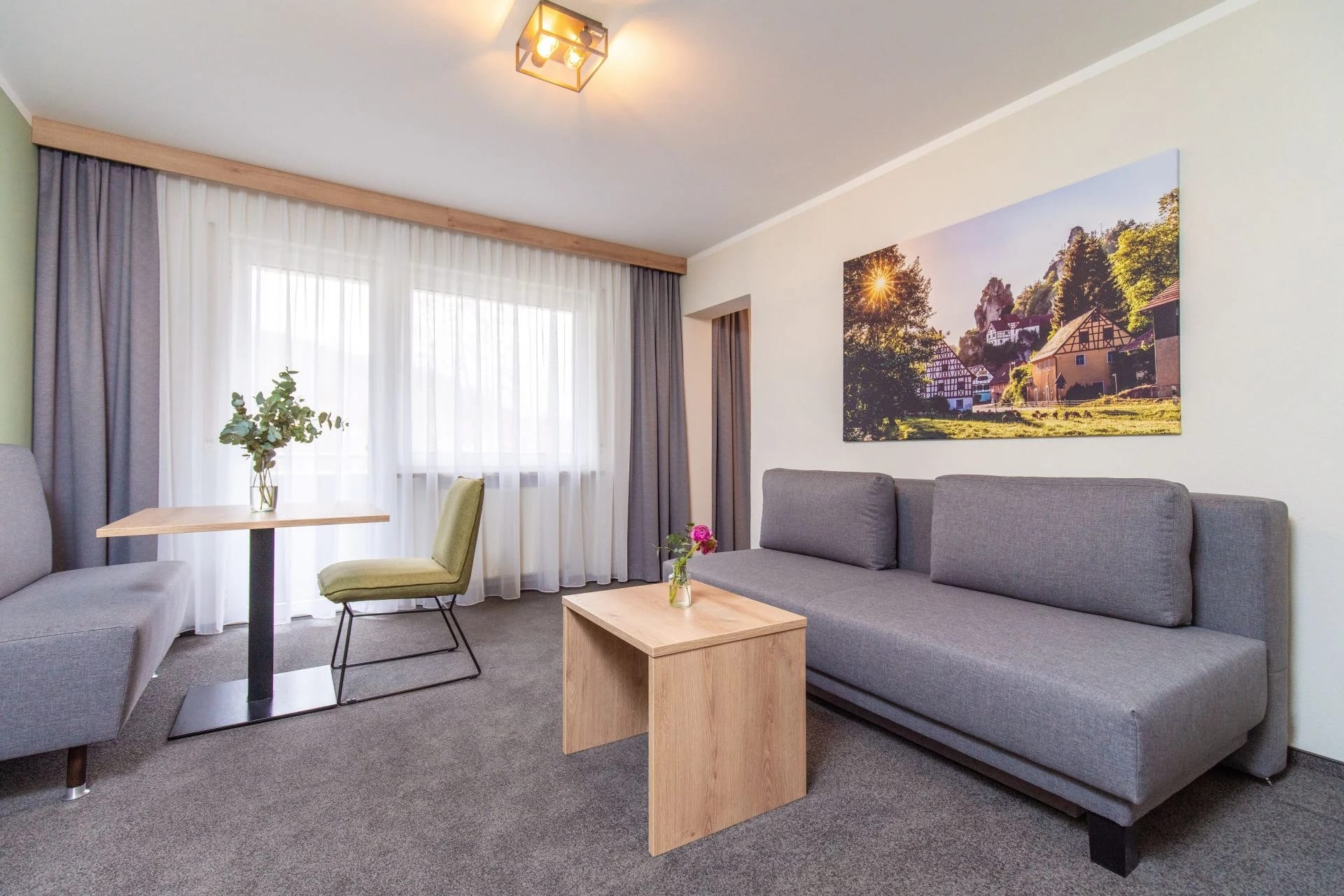 Wohnbereich der Suite mit grauem Sofa, Couchtisch, Sessel und kleinem Tisch am Fenster