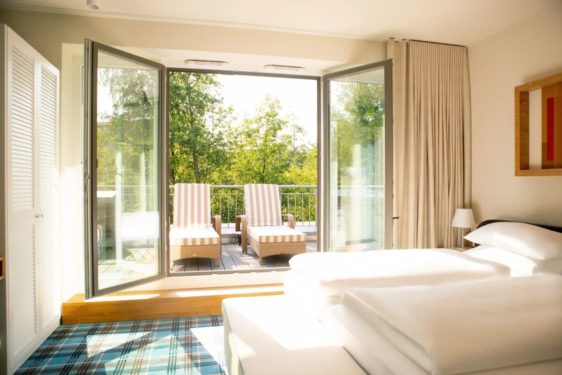 Schlafzimmer mit weit geöffneter Balkontür, zwei Liegestühlen auf dem Balkon und Blick ins Grüne