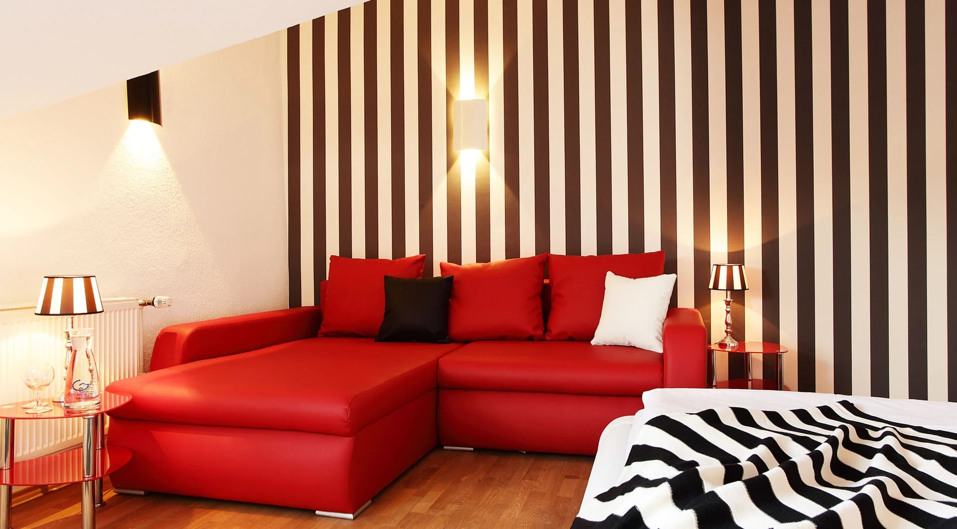 Zimmer mit rotem Ecksofa vor gestreifter Wand und Zebra-Bettwäsche