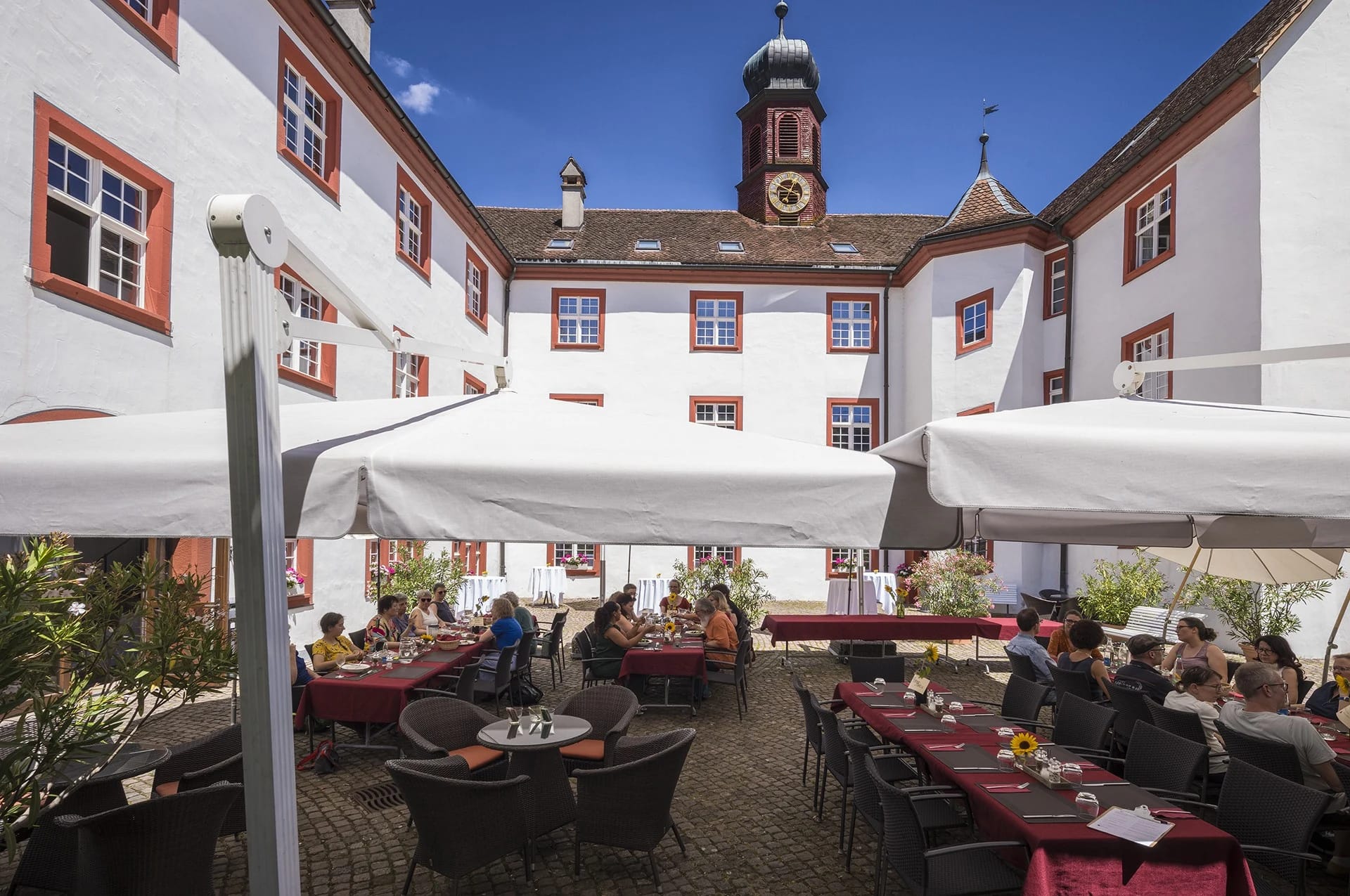 Terrasse im Innenhof mit Sonnenschirmen und Sitzplätzen vor dem Klostergebäude mit Turm