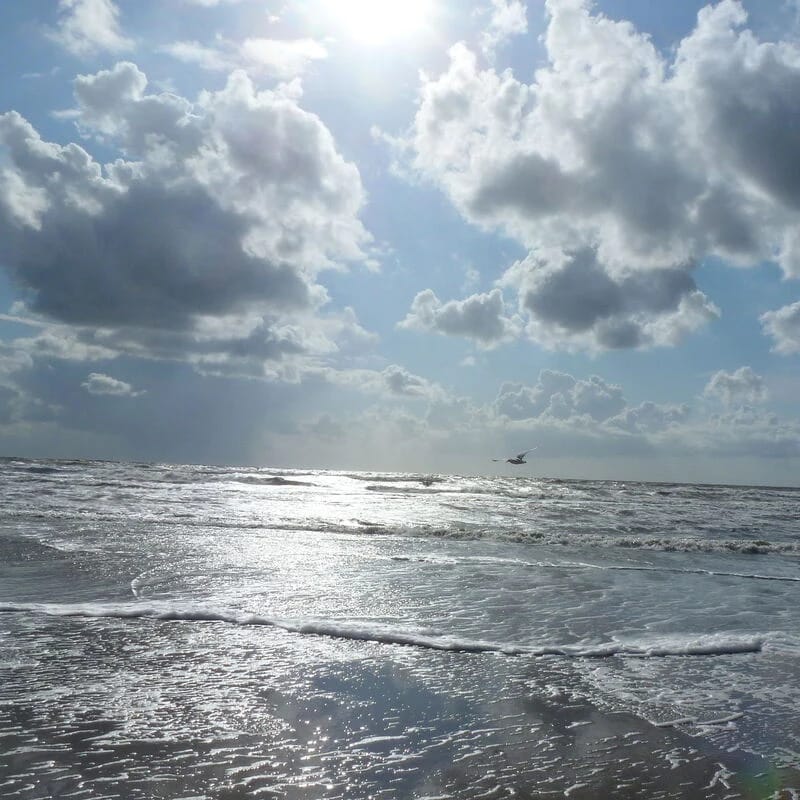 Sonne bricht über der Nordsee durch die Wolken, Wellen laufen auf den nassen Strand