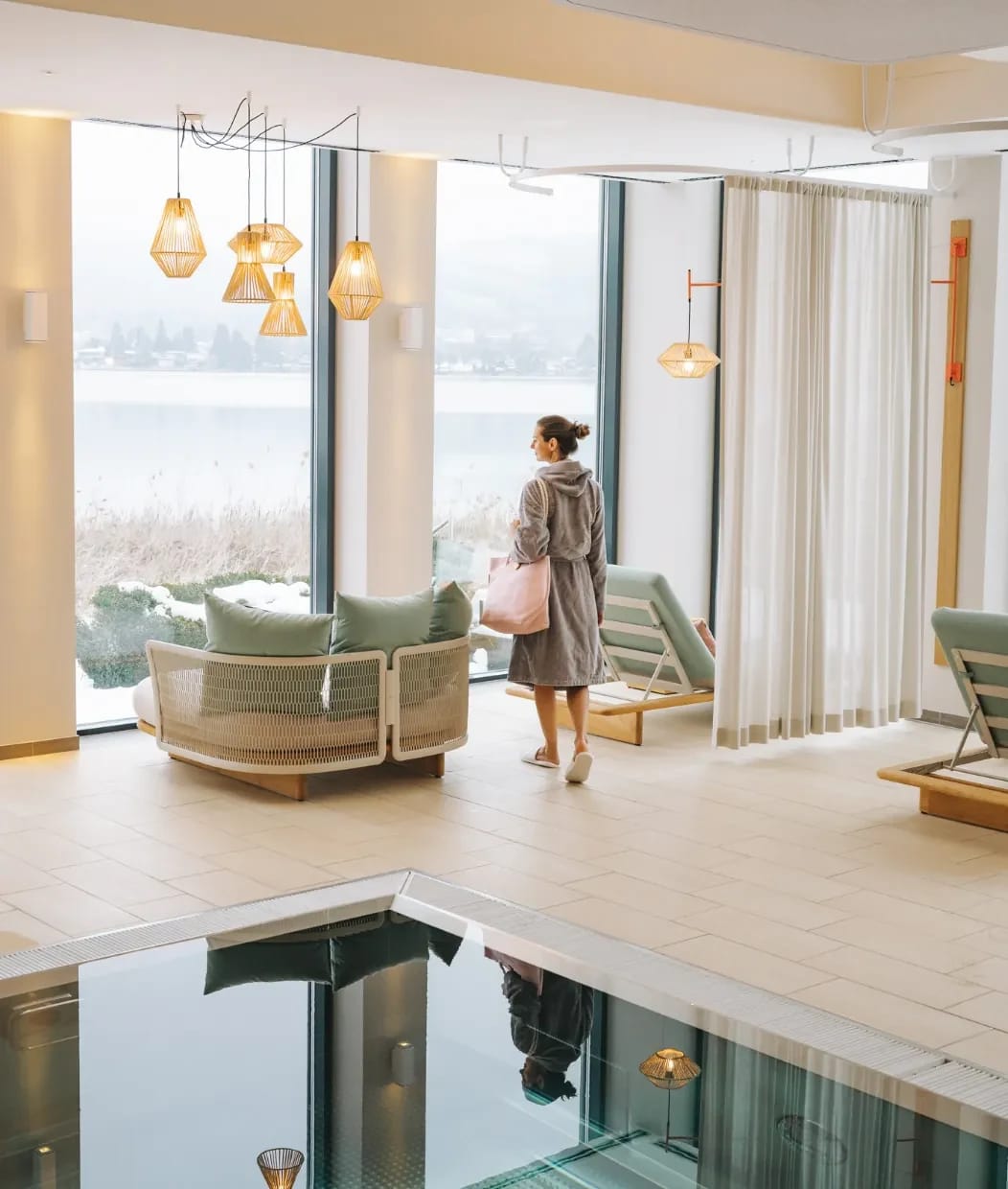 Innenpool im Wellnessbereich mit Ruheliegen, Korbsessel und raumhohen Fenstern zum See