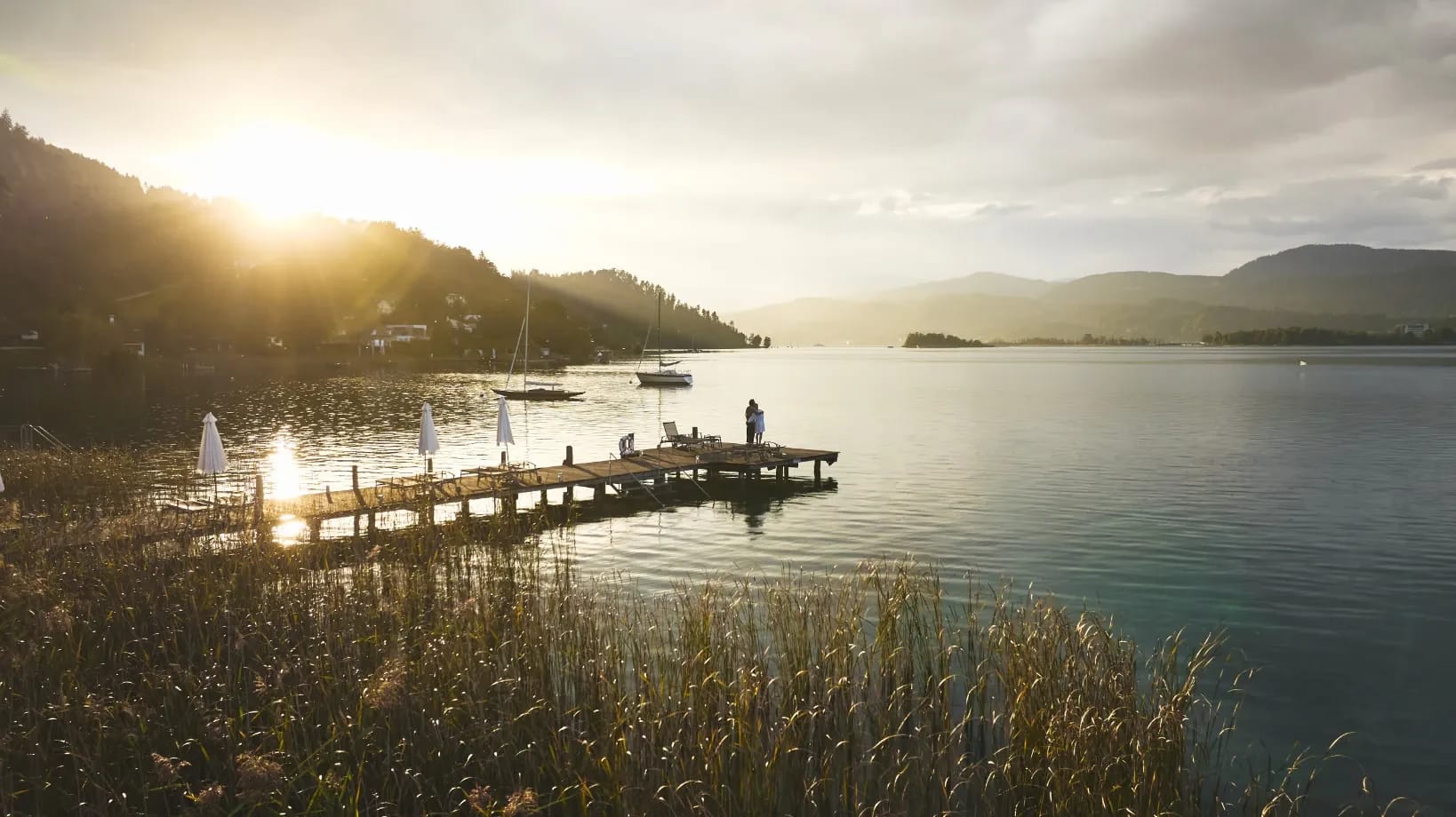 Sonnenuntergang über dem Wörthersee, im Vordergrund der Badesteg mit Sonnenschirmen zwischen Schilf