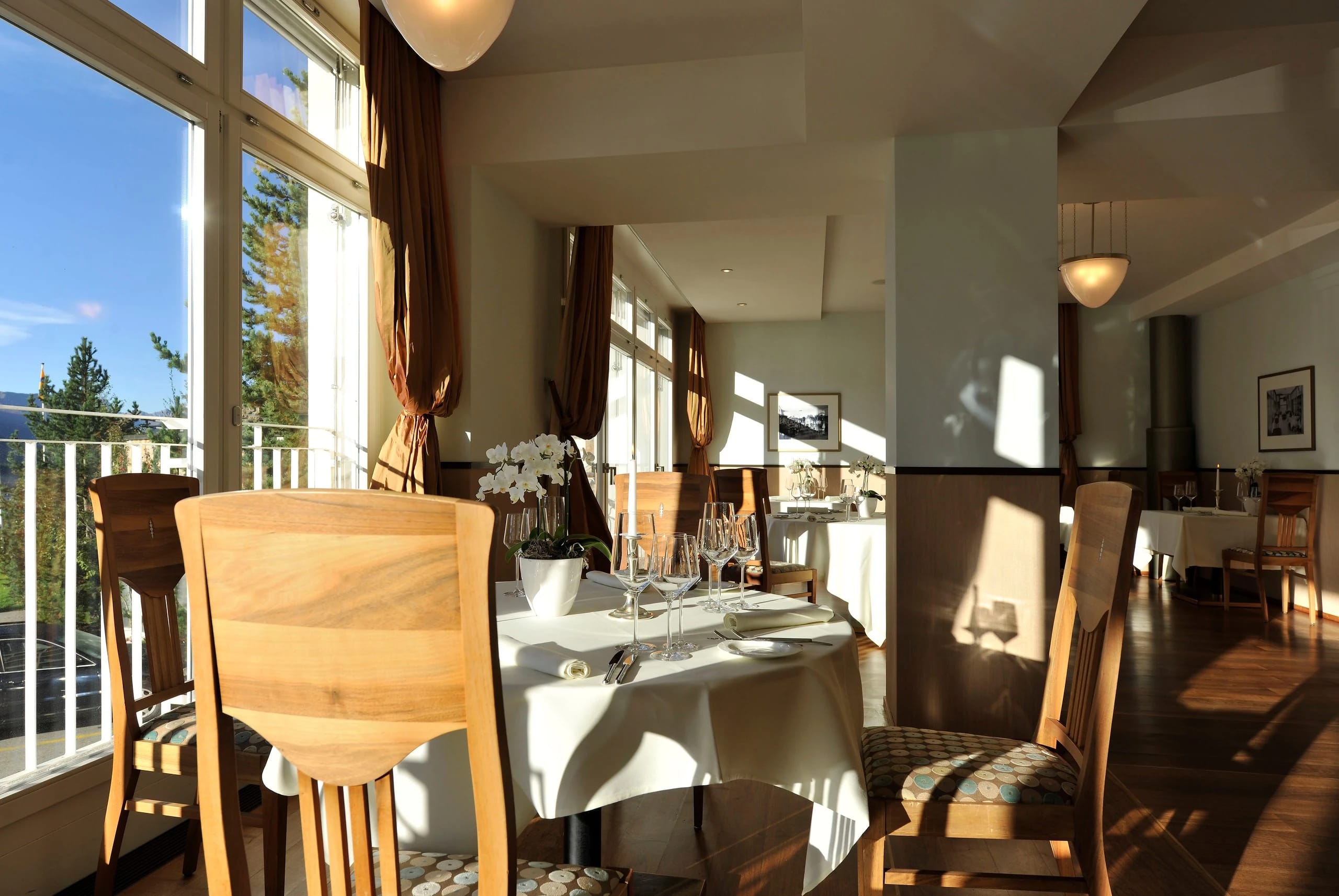 Restaurant mit eingedecktem Tisch am Fenster, Holzstühlen und Sonnenlicht, Blick ins Grüne