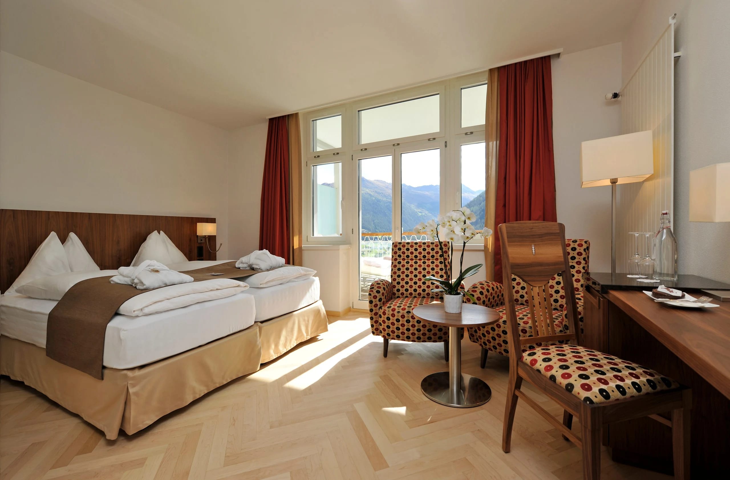 Sonnendurchflutetes Doppelzimmer mit zwei Betten, Sitzecke, Schreibtisch und Fenster mit Bergblick