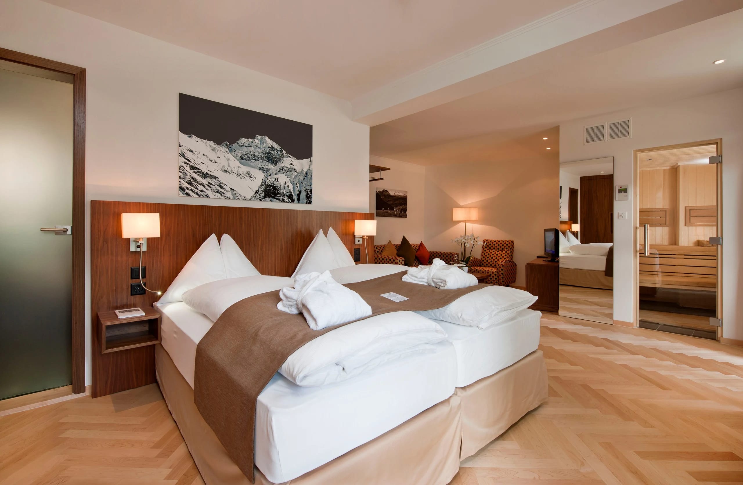 Junior-Suite mit Doppelbett, Bergfoto über dem Bett und angrenzendem Raum mit Sauna