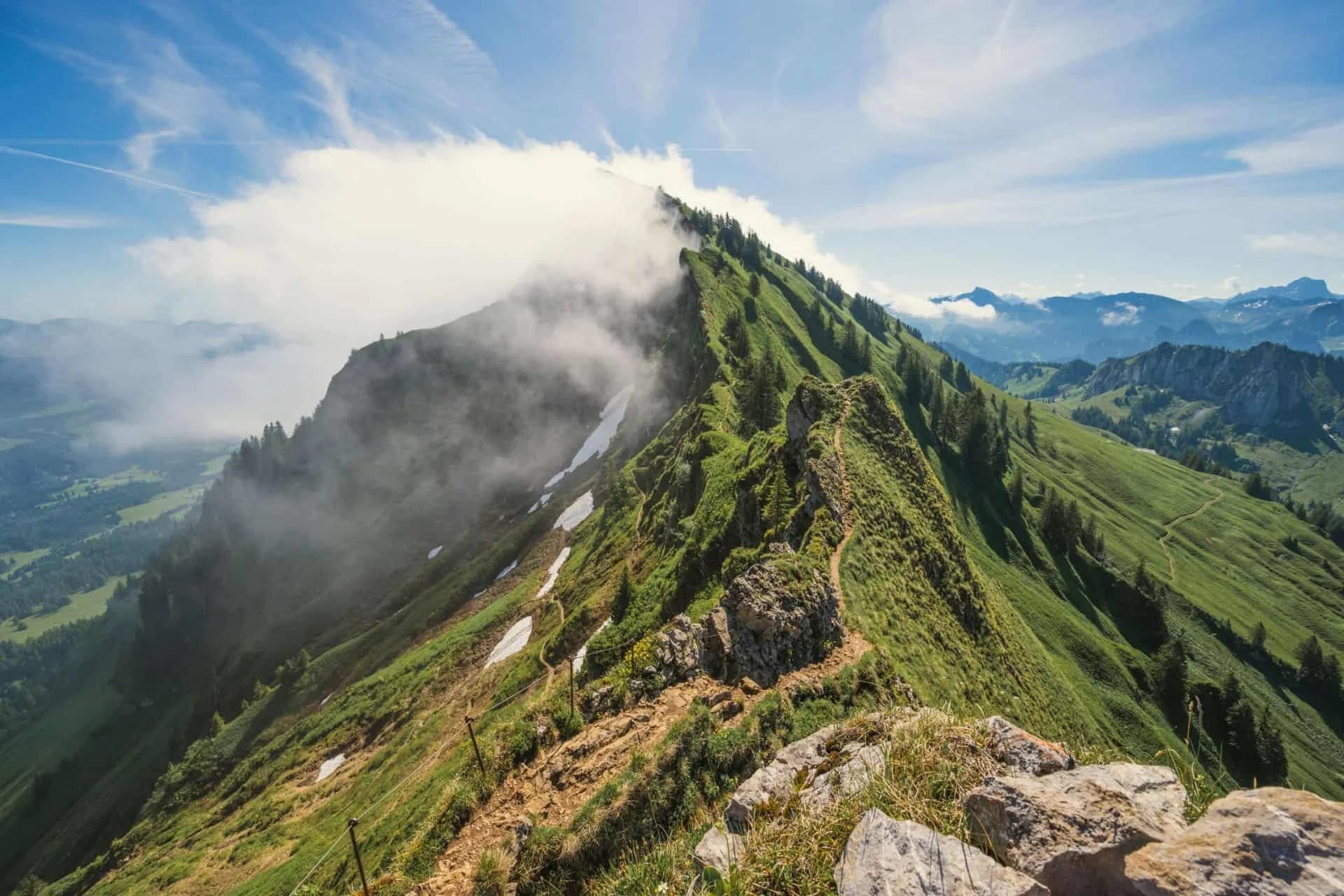 Wanderweg über einen grünen Bergkamm mit aufziehenden Wolken