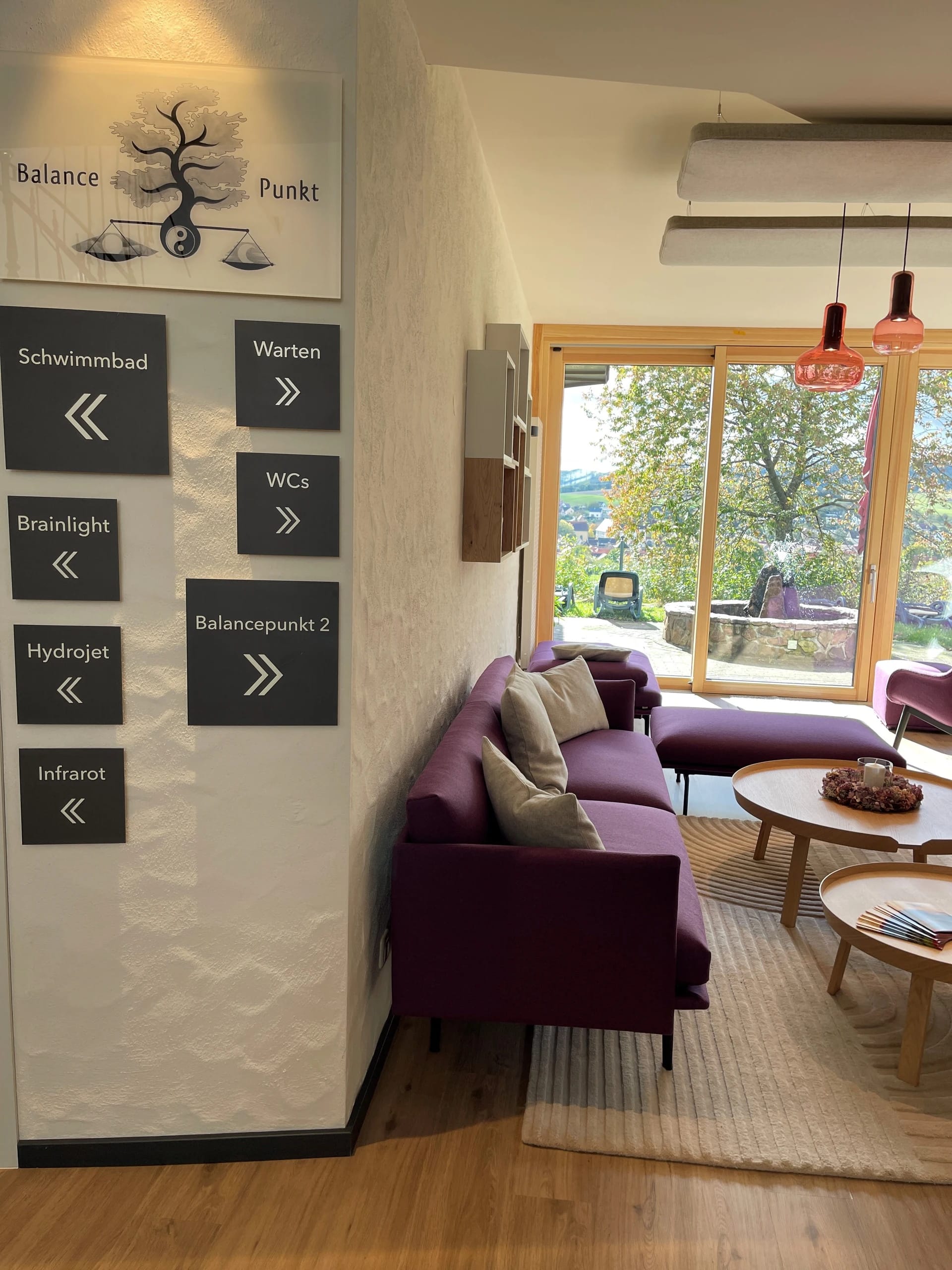 Wartebereich im Wellnessbereich mit violetten Sofas, Wegweisertafeln und Fenster zur Terrasse