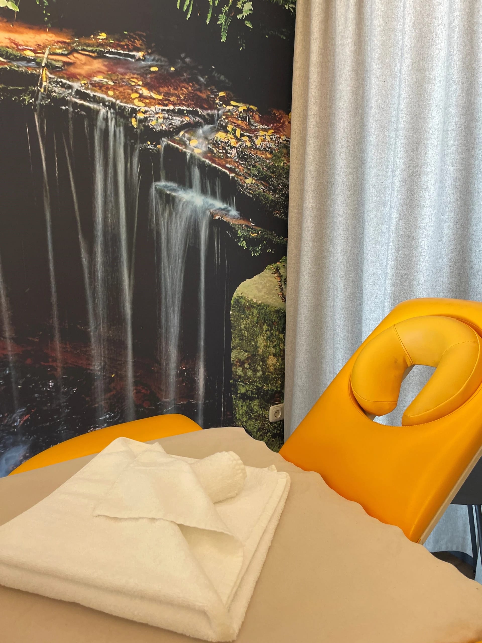 Massageraum mit Liege, gefalteten Handtüchern und Wasserfall als Fototapete