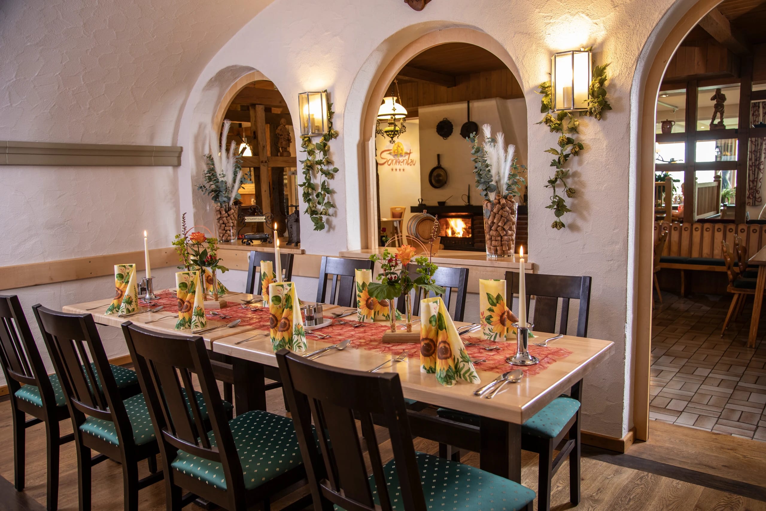 Weinstube mit gedeckter Tafel, Rundbögen und Kaminfeuer im Hintergrund